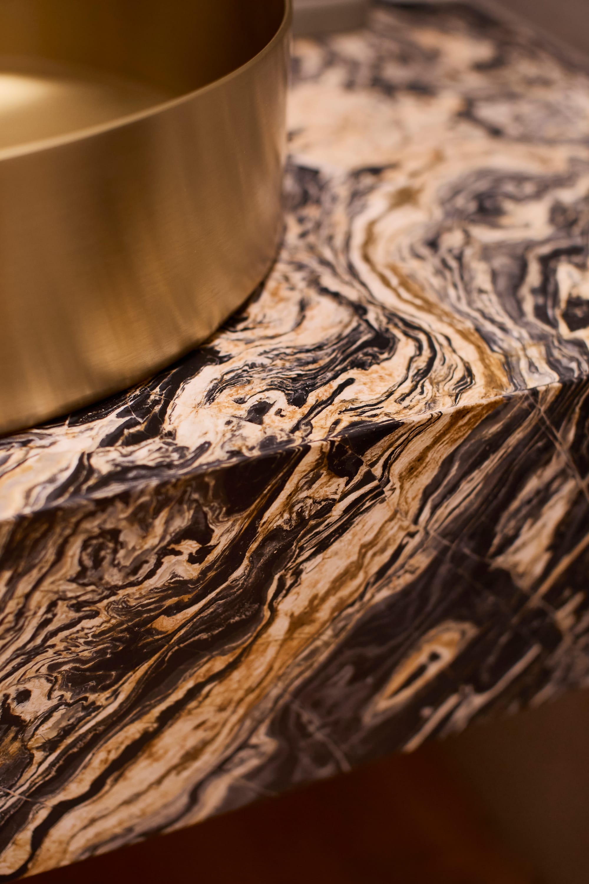 Brixton by Cera Stribley. Photography by Martina Gemmola. Close-up of a luxurious swirled marble countertop with dramatic veining, paired with a brushed brass vessel basin.