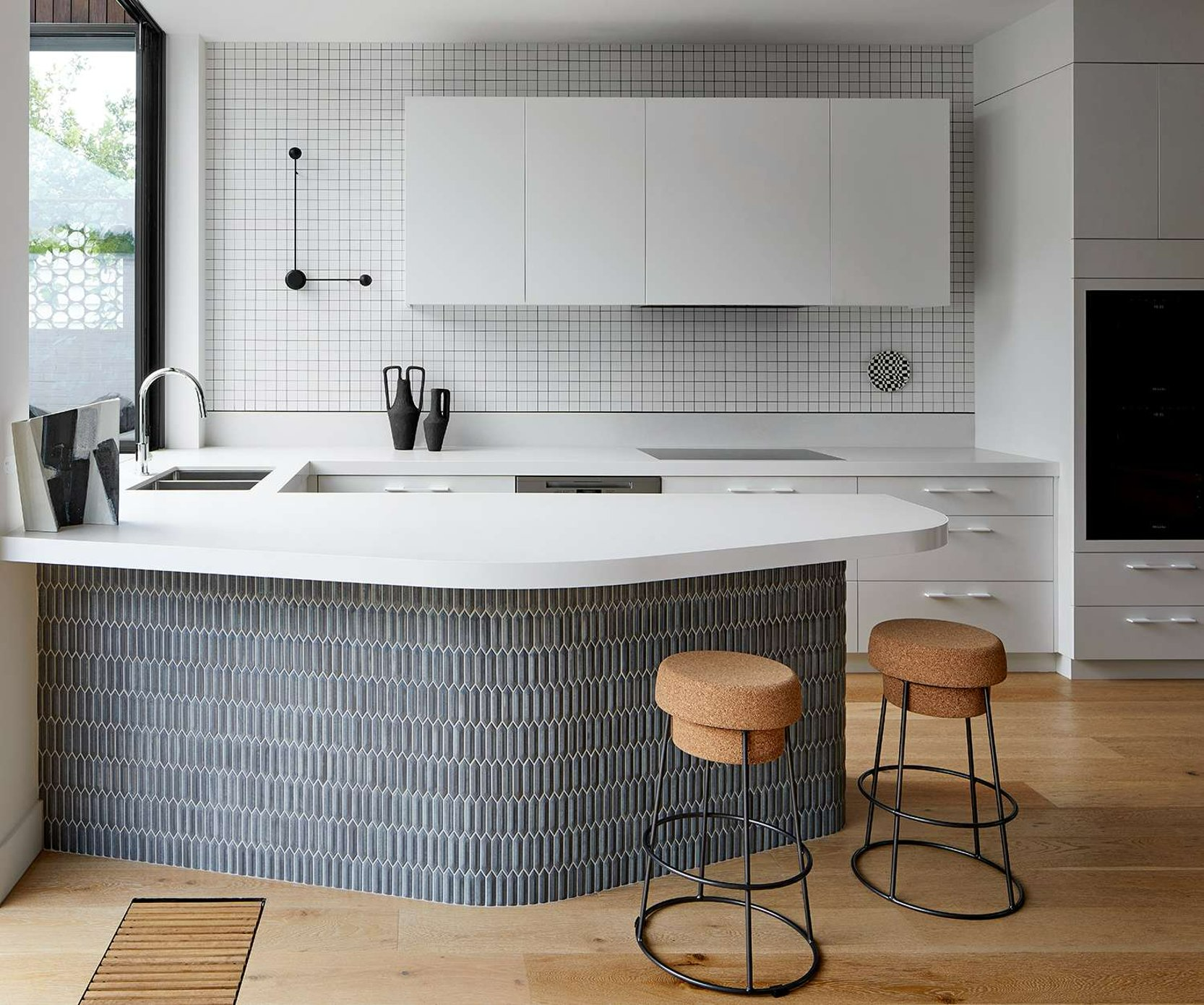 Neville St Residence by Chan Architecture. Photography by Tatjana Plitt. Kitchen with tiled island bench, cork stools, tiled splashback and timber floors. 