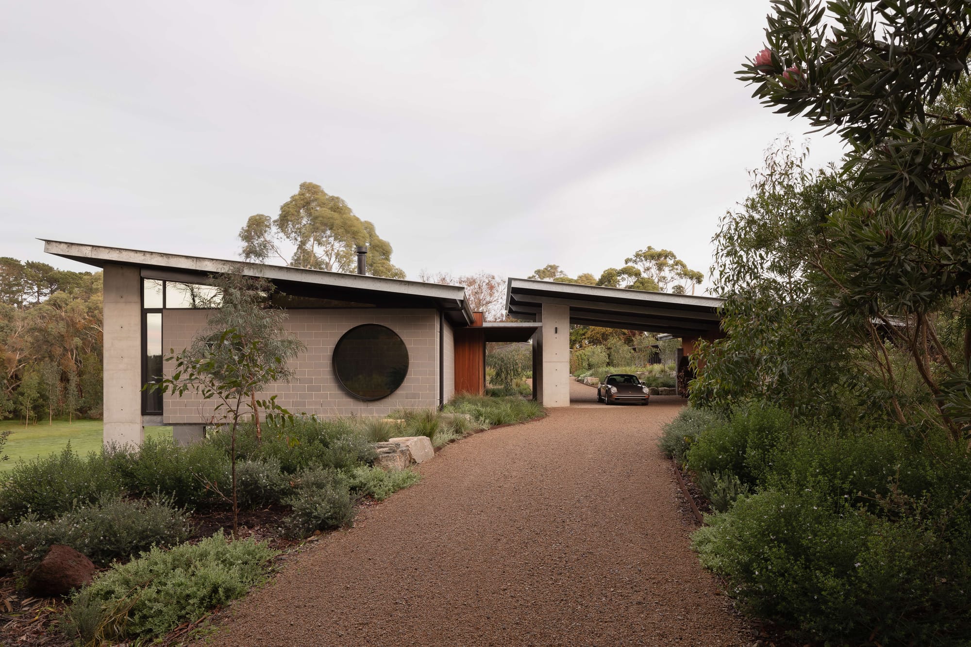 Merricks House by Aktis Architects. Photography by Timothy Kaye. Modern carport with timber and blockwork walls, circular window, and pitched metal roof sheltering a vintage Porsche.