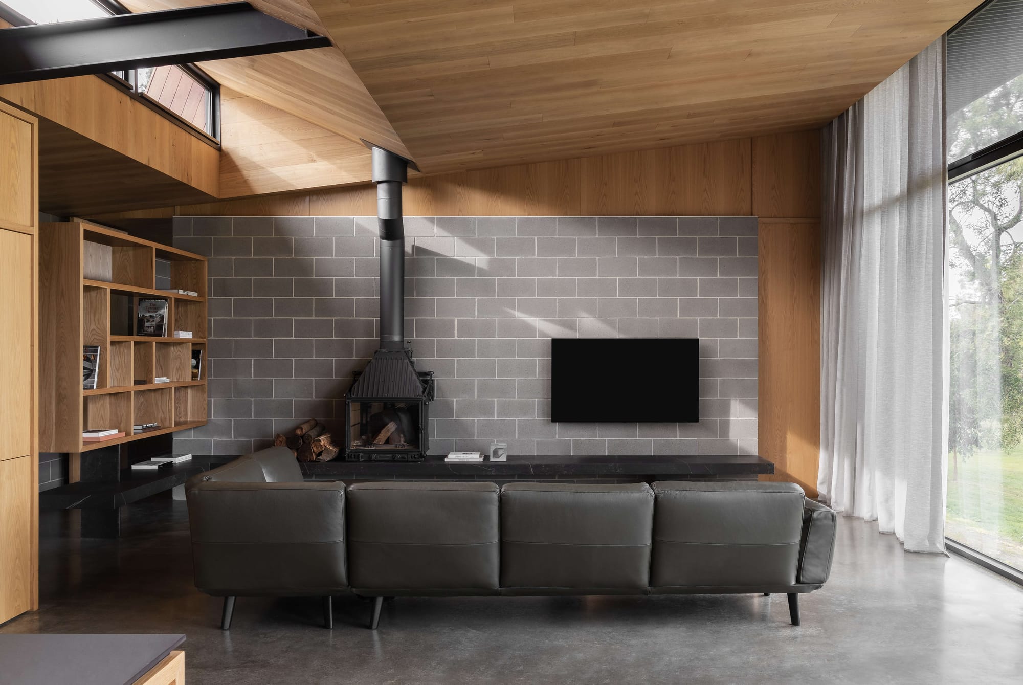 Merricks House by Aktis Architects. Photography by&nbsp;Timothy Kaye. Modern living room with concrete block feature wall, black wood-burning stove, leather sofa, timber shelving, and floor-to-ceiling windows.