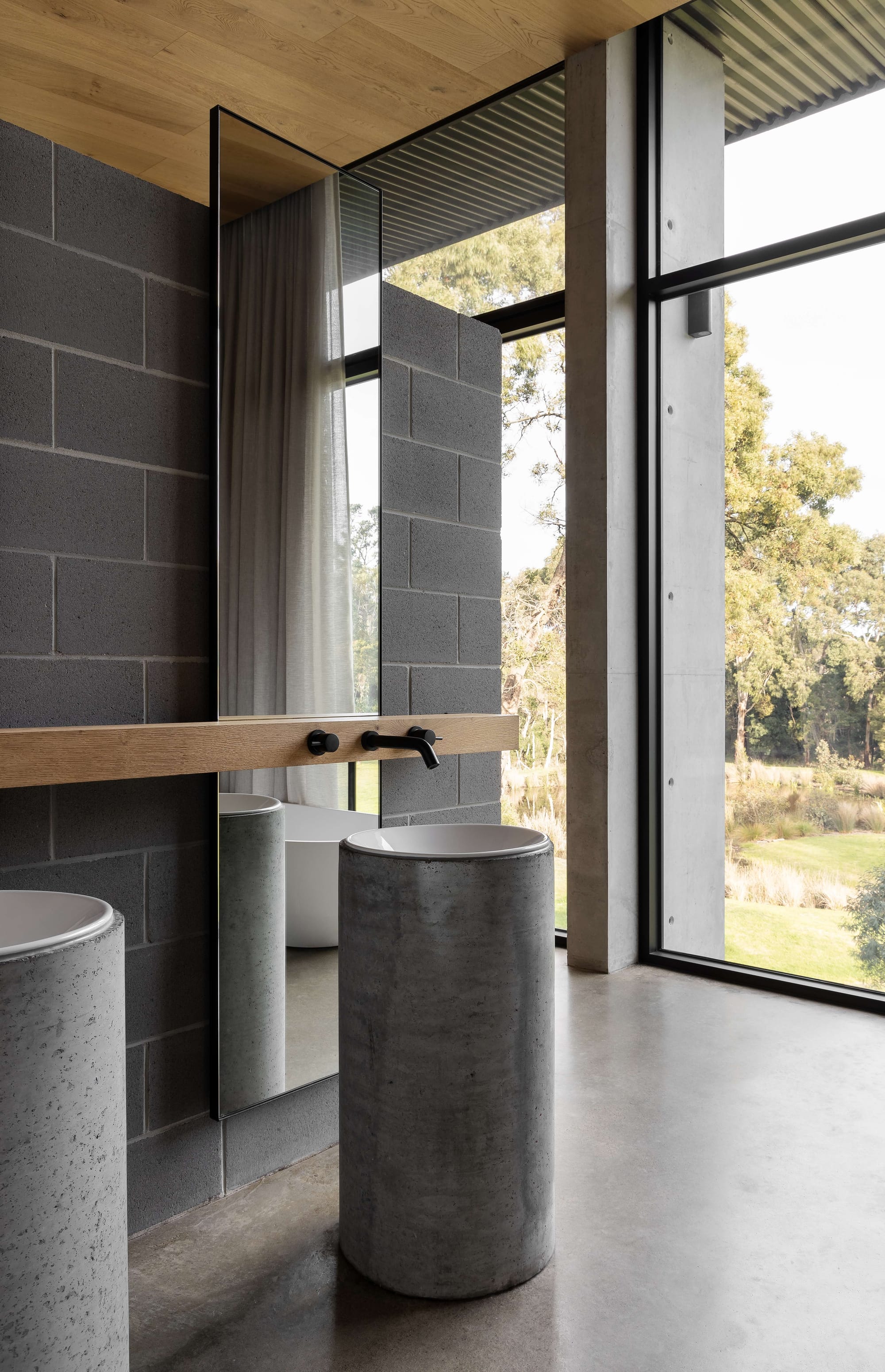 Merricks House by Aktis Architects. Photography by&nbsp;Timothy Kaye. Modern bathroom with cylindrical concrete basins, full-height mirror, blockwork walls, and expansive windows overlooking a natural landscape.