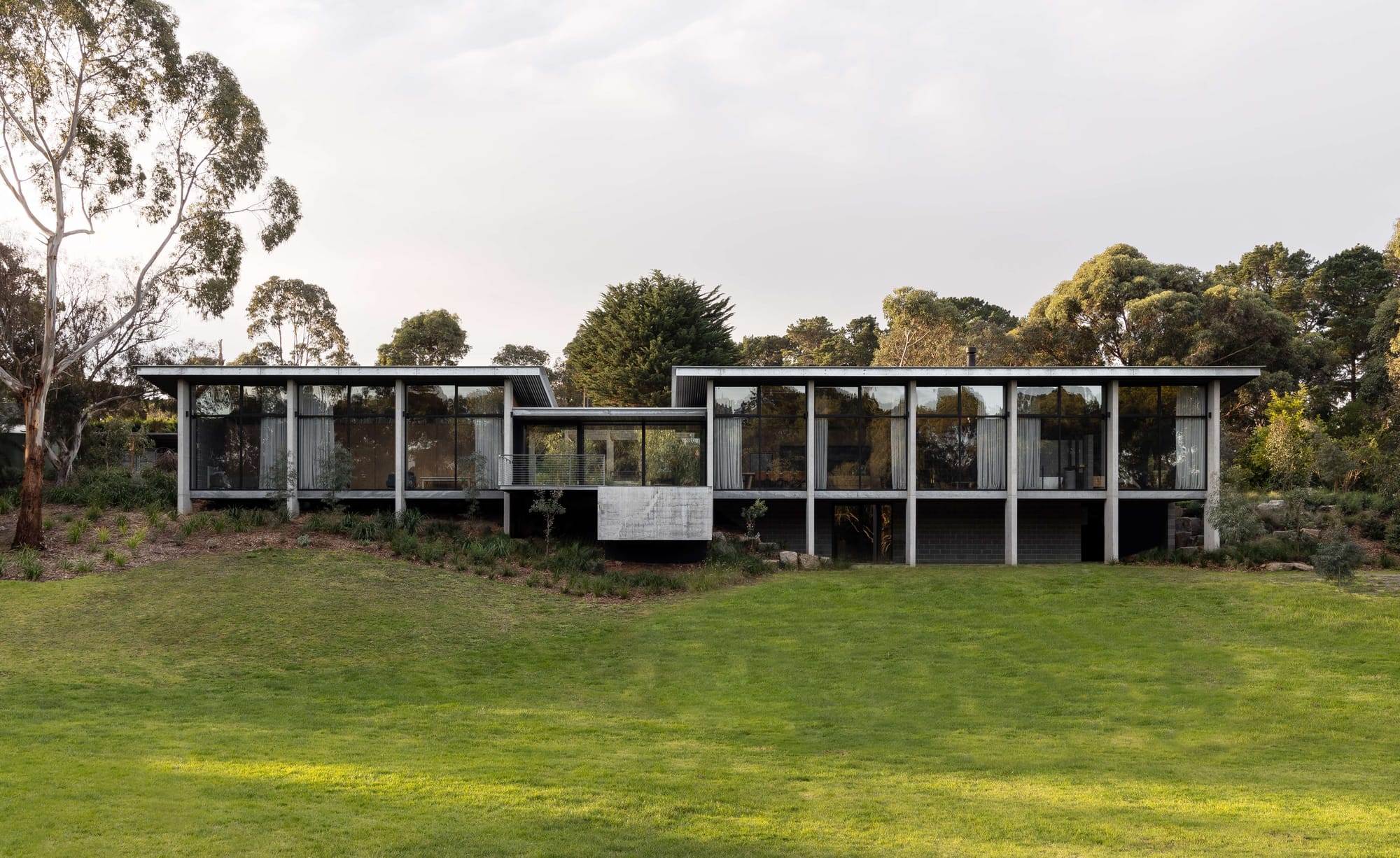 Merricks House by Aktis Architects. Photography by&nbsp;Timothy Kaye.Expansive modern home with a rhythmic concrete and glass facade, elevated on a slope amidst natural bushland.