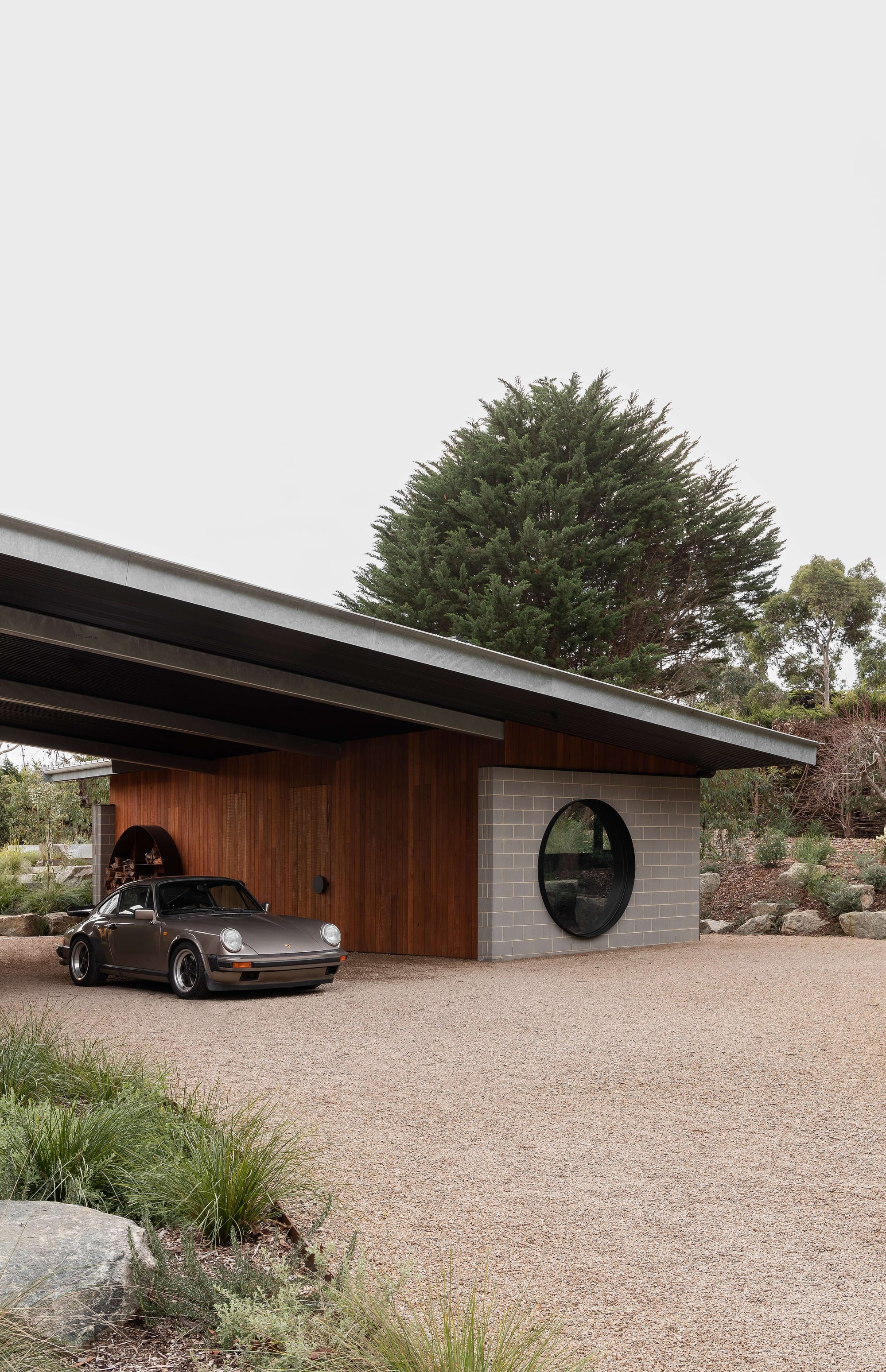 Merricks House by Aktis Architects. Photography by&nbsp;Timothy Kaye. Modern carport with timber and blockwork walls, circular window, and pitched metal roof sheltering a vintage Porsche.