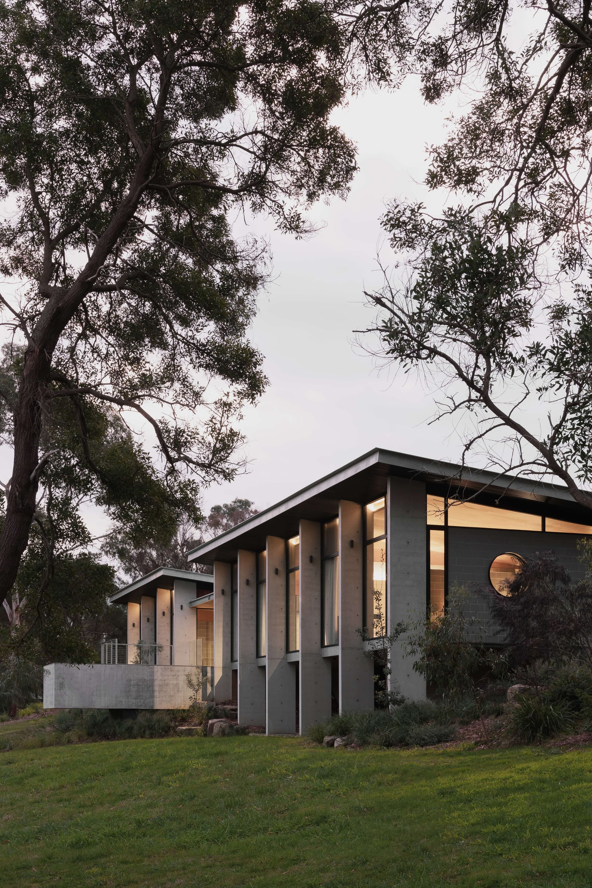 Merricks House by Aktis Architects. Photography by&nbsp;Timothy Kaye.Modern concrete house with narrow vertical fins and clerestory glazing, framed by native trees and evening light.