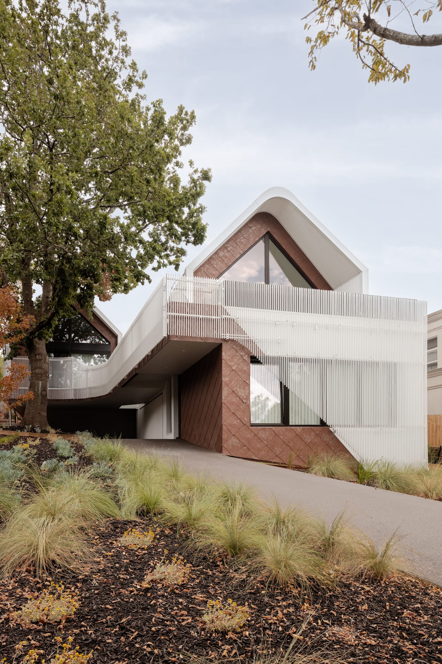 TREE HOUSE by R Architecture. Photography by CM Photography. Double Storey home with concrete driveway with white faced balcony and terracotta colored wall tile.