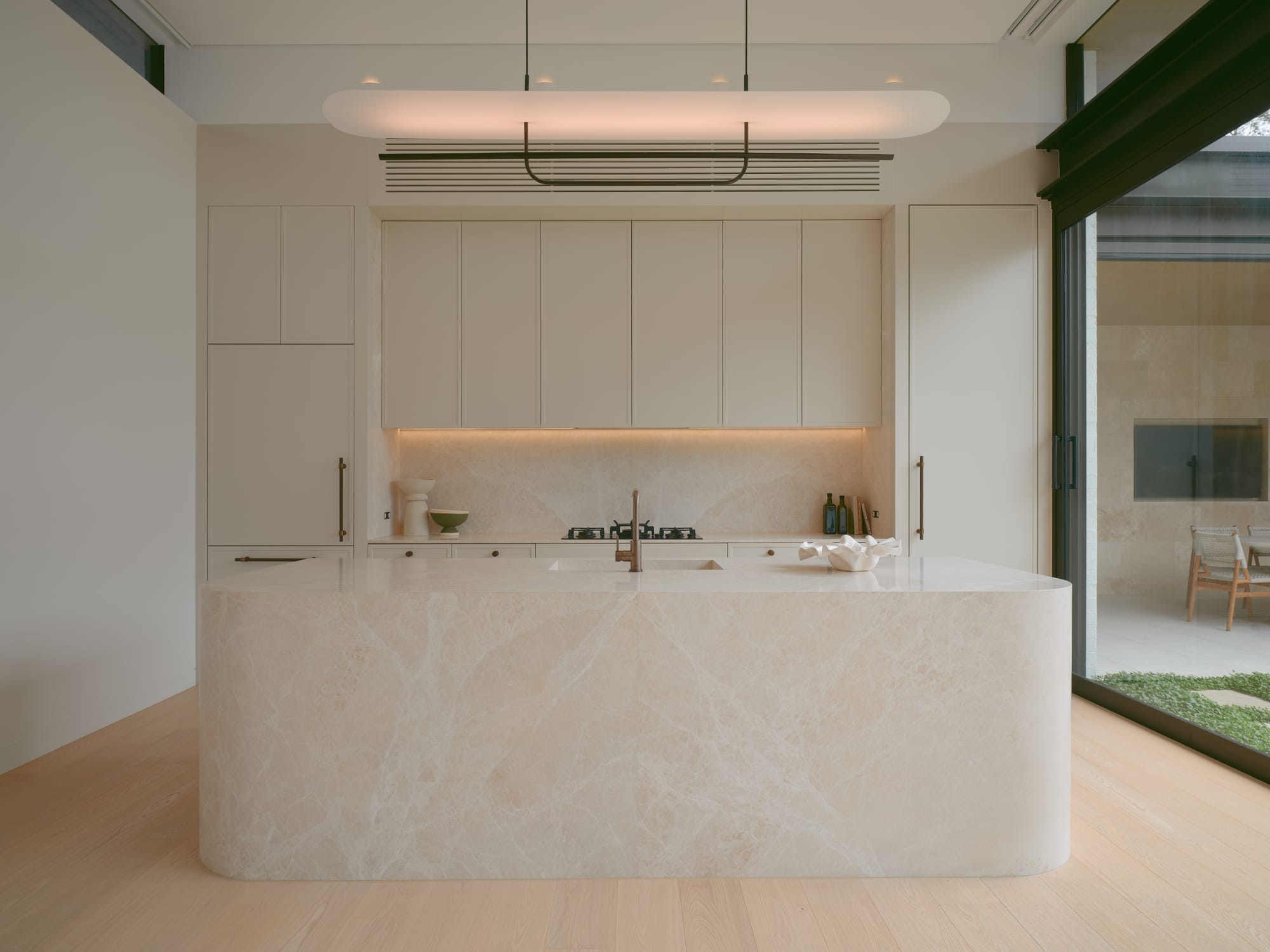 Sole House by 868 Architects. Photography by Martin Siegner. Contemporary kitchen with a sculpted marble island, minimalist cabinetry, integrated appliances, and large glass doors offering seamless indoor-outdoor connection.