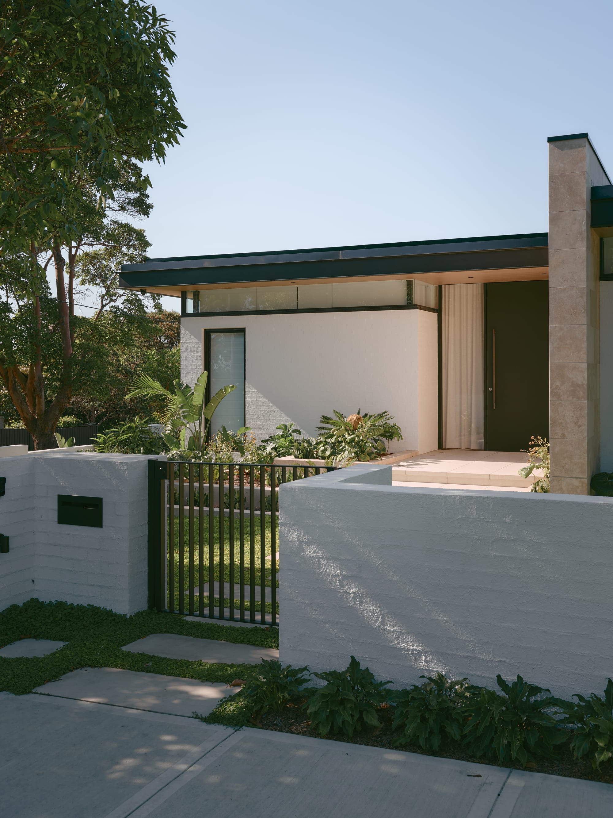 Sole House by 868 Architects. Photography by Martin Siegner. Modern white house with flat roof, black-framed windows, and lush garden behind a white wall and gate.