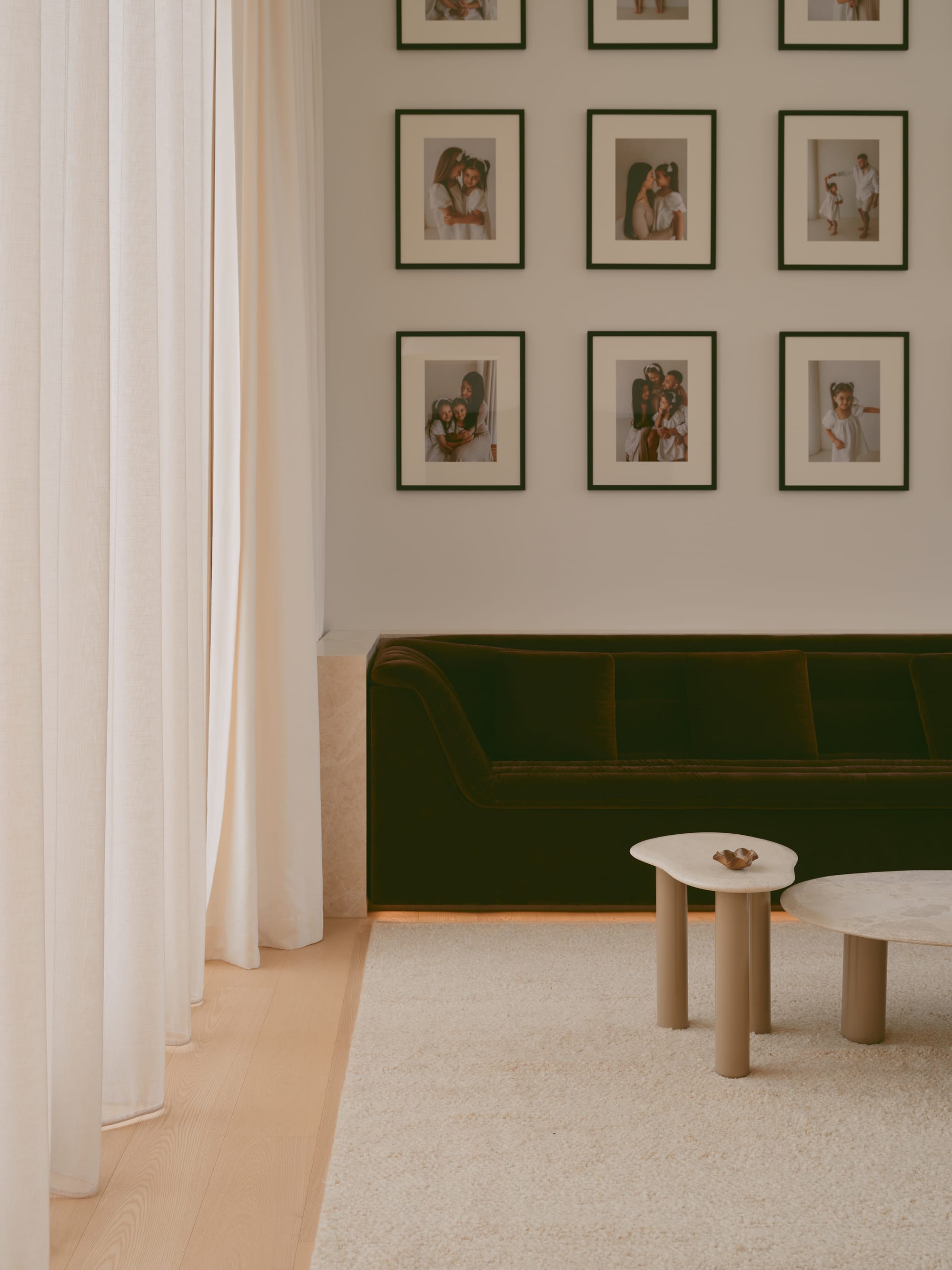Sole House by 868 Architects. Photography by Martin Siegner. Stylish living room corner with a dark velvet sofa, creamy sheer curtains, sculptural nesting coffee tables, and a gallery wall of framed family portraits.