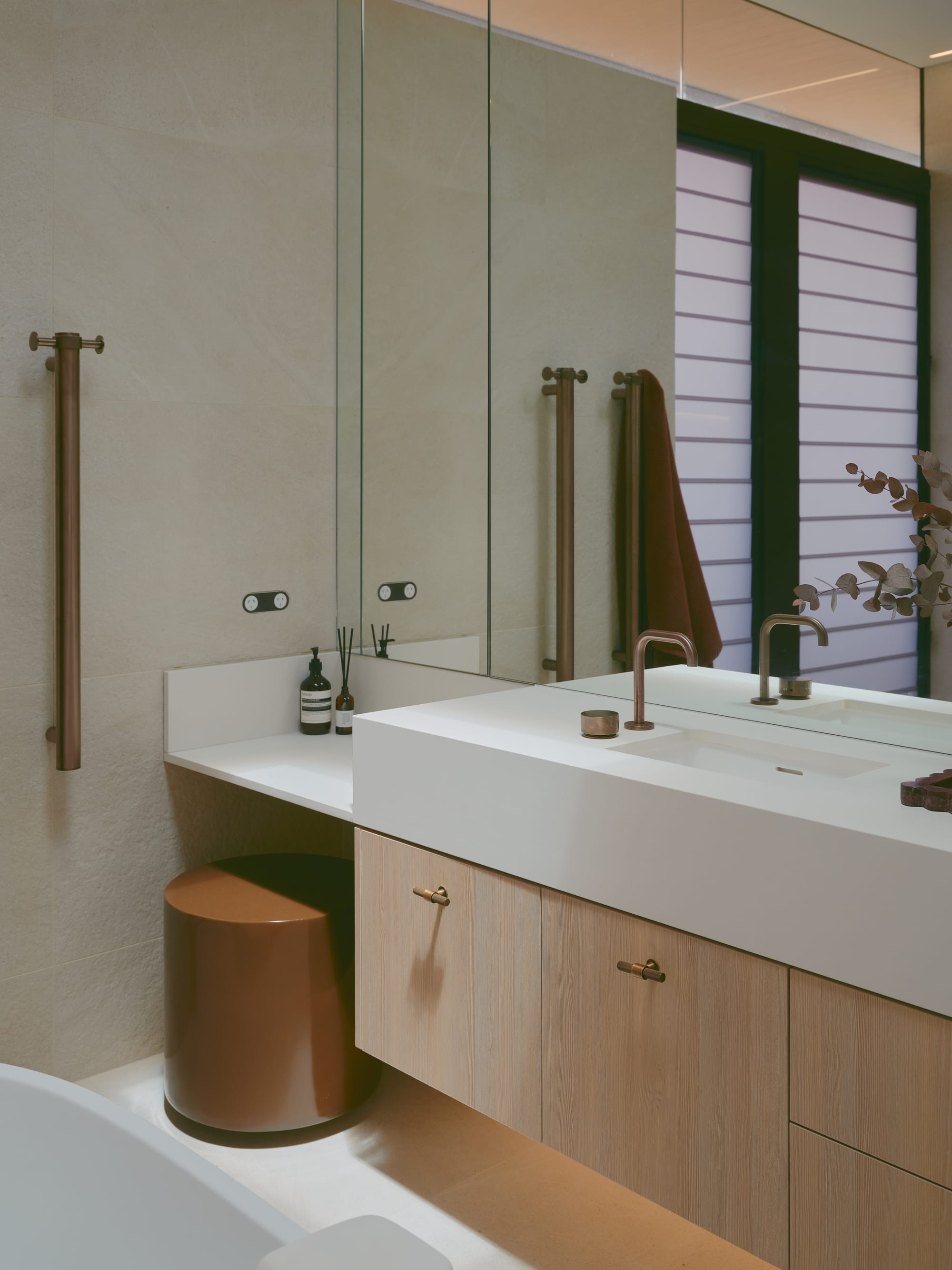 Sole House by 868 Architects. Photography by Martin Siegner. Elegant bathroom with a floating vanity, matte bronze fixtures, large mirror cabinetry, and a soft neutral palette accented by warm lighting and minimalist decor.