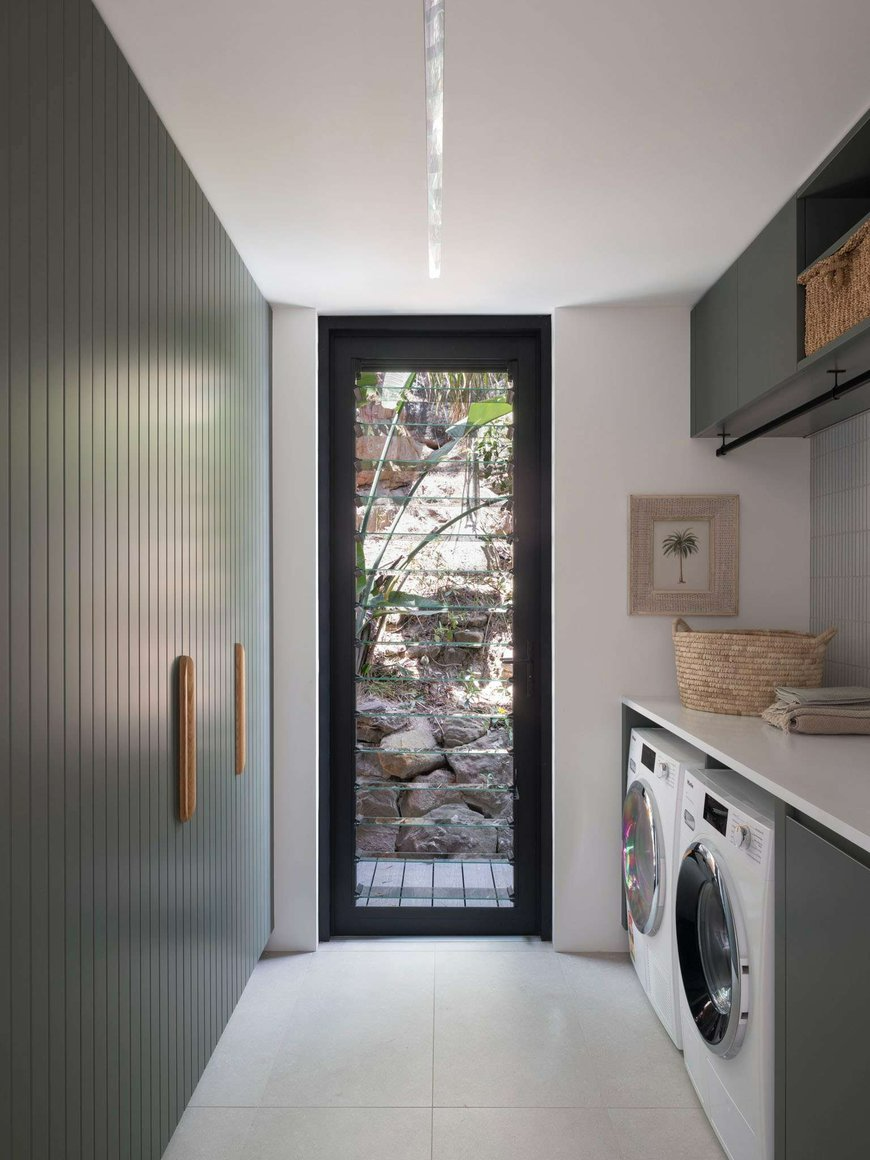 Palm Beach 01 by Watershed Architects. Photography by Tom Ferguson. Laundry with sage green full height cupboard on the left and bench on right, with front loader machines and white countertops. 