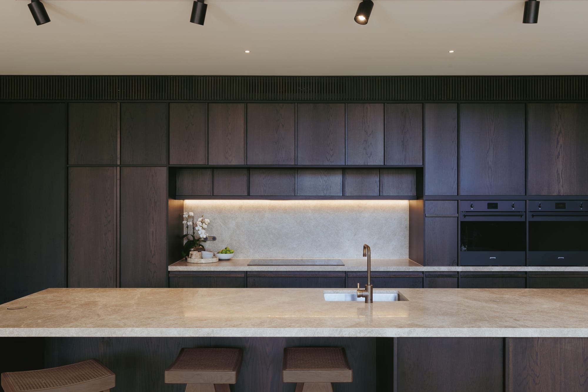 Little Birch by buck&simple. Photography by Tim Pascoe. Kitchen with dark timber veneer on cabinets, beige stone countertops and splashbacks.