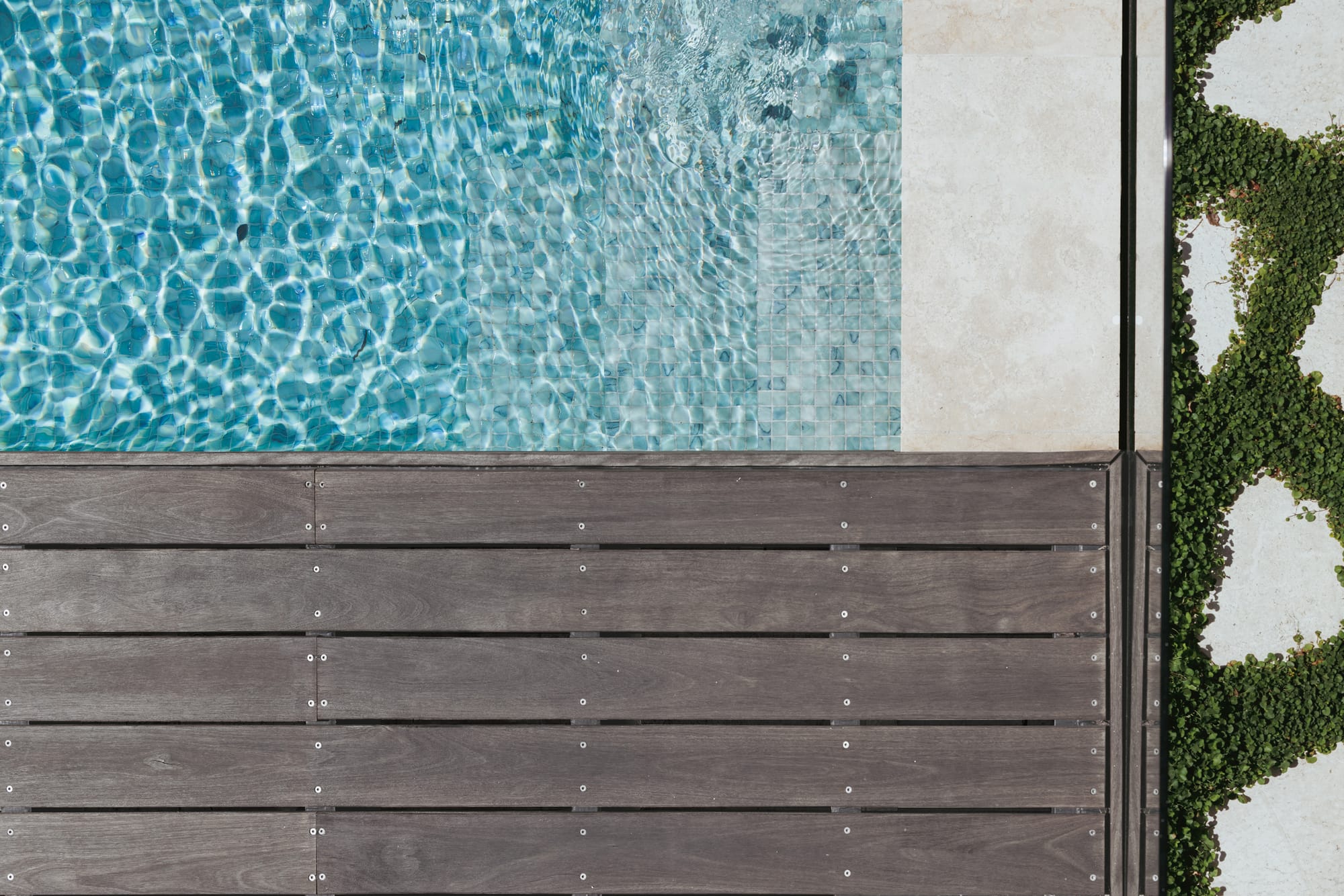 Little Birch by buck&simple. Photography by Tim Pascoe. Birds eye view of timber decking extending over blue, mosaic tiled pool with cream tiling around pools edge. 