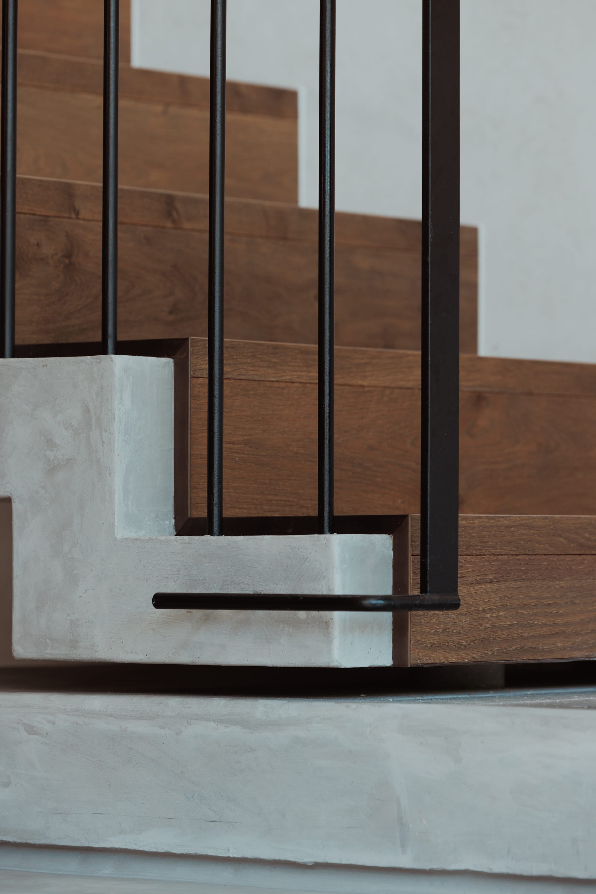 Little Birch by buck&simple. Photography by Tim Pascoe. Close-up detail shot of black metal handrail connecting to concrete portion of staircase, with timber steppers.