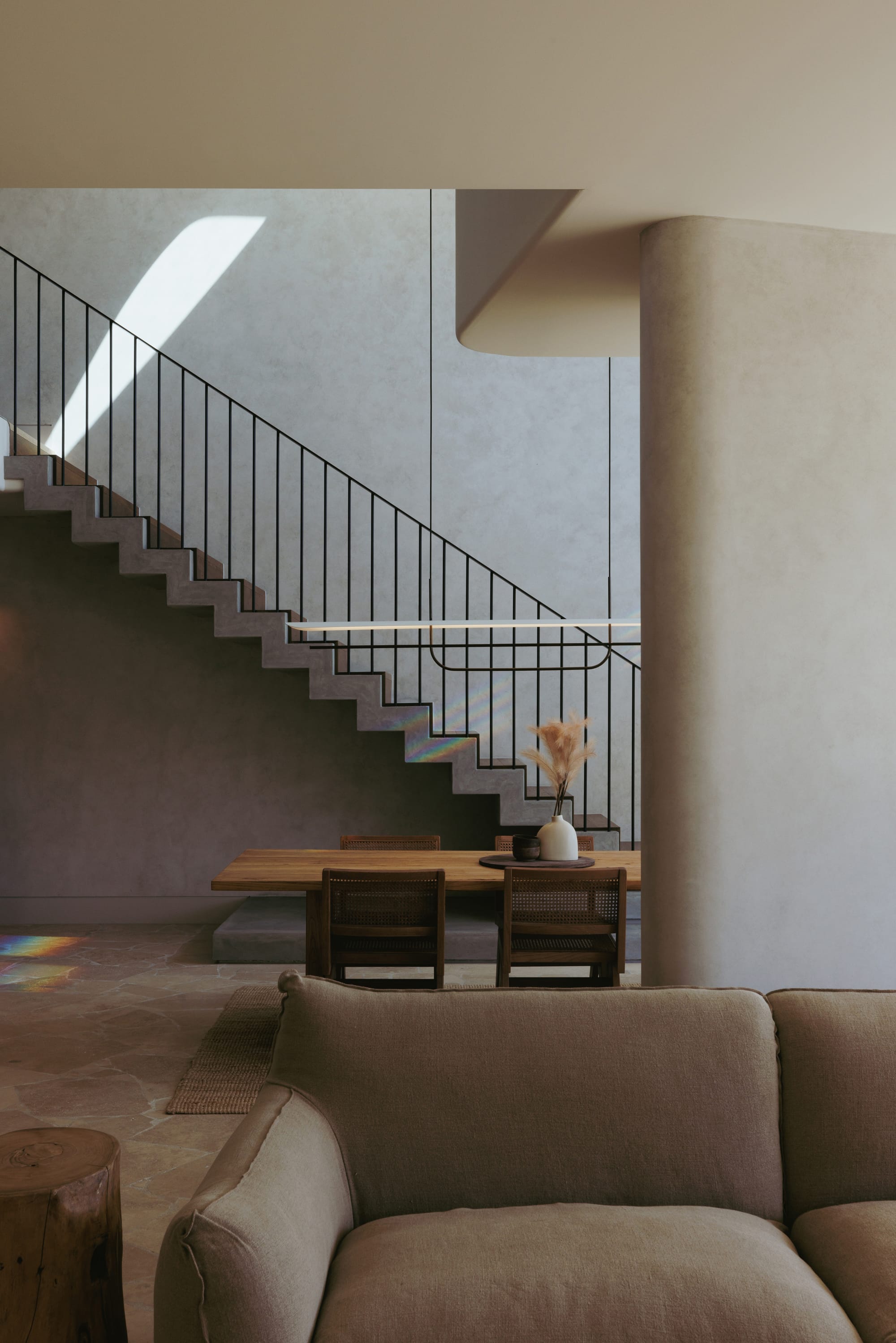 Little Birch by buck&simple. Photography by Tim Pascoe. Open plan living and dining space with brown, modular couch, timber side table, timber dining table and concrete stairs. 