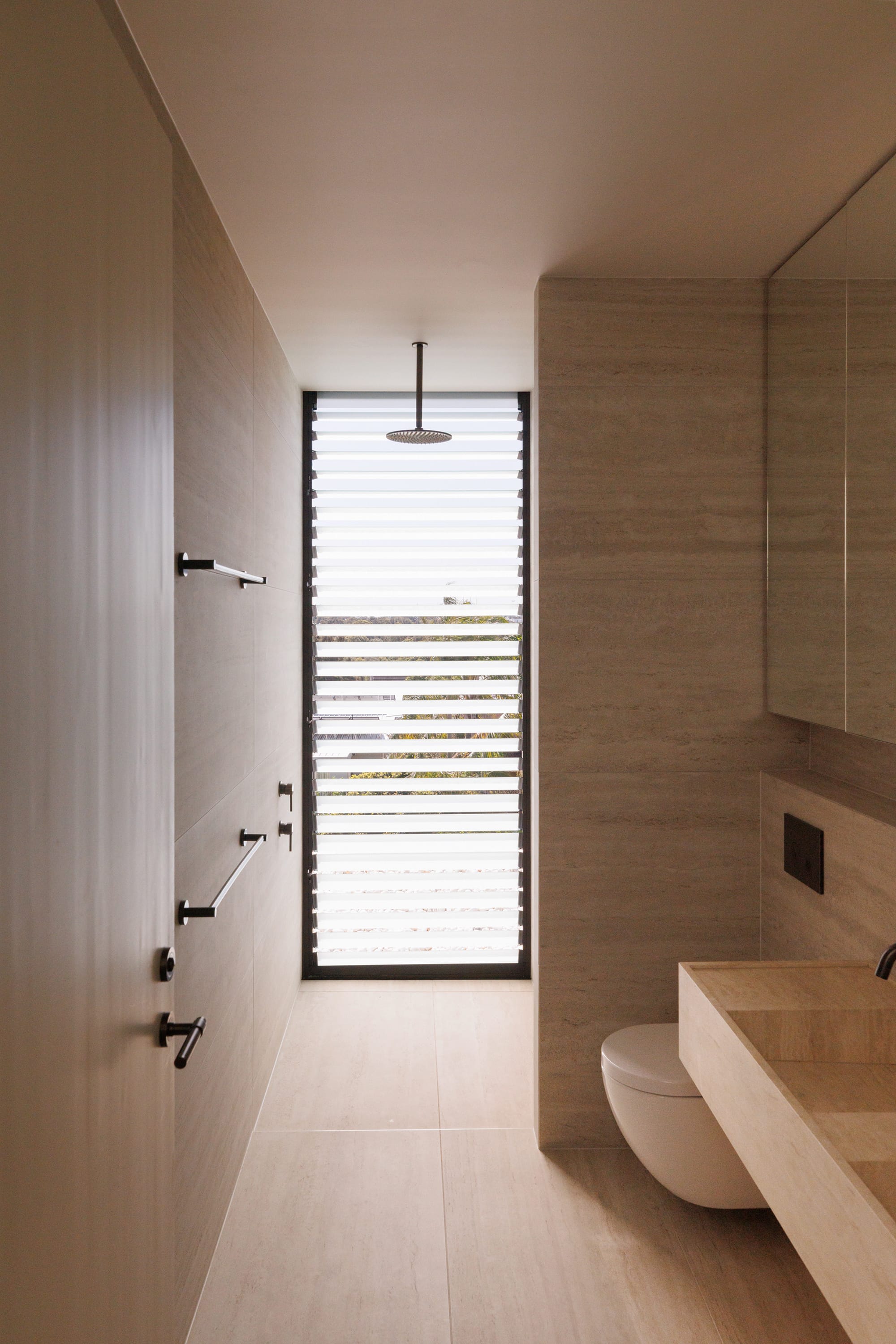 Little Birch by buck&simple. Photography by Tim Pascoe. Bathroom with sandstone tile on floor, walls and sink, with louvered window and rainfall shower head. 
