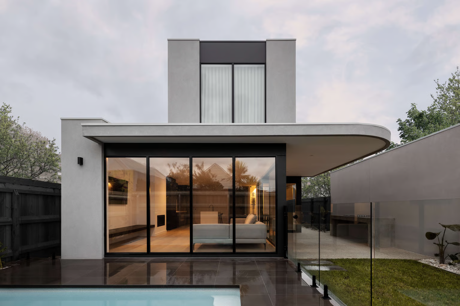 Anderson Street Newport by Mancini Made. Photography by Timothy Kaye.Modern two-storey home with curved cantilevered roof, floor-to-ceiling glass doors, and a sleek poolside patio.