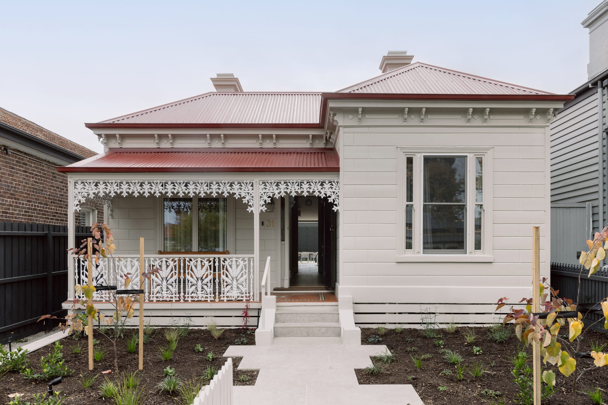 Auburn Residence by Chan Architecture. Photography by Elise Scott. Street facade of double-front Victorian home with white clad exterior, ornate balustrade around patio and red tin roof. 