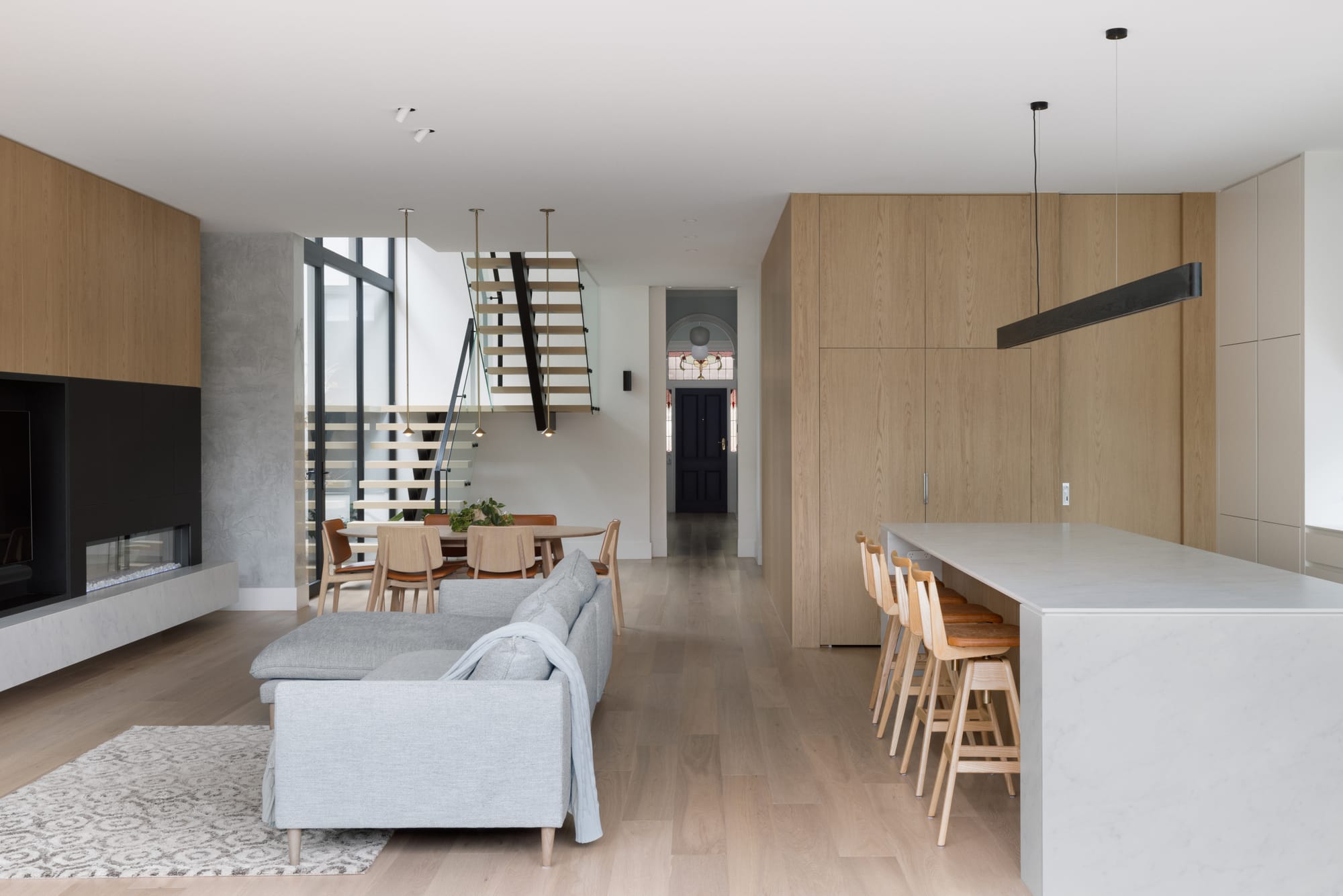Auburn Residence by Chan Architecture. Photography by Elise Scott. Open plan kitchen, living and dining area with timber flooring and joinery, lighting finishes and a staircase in the background. 