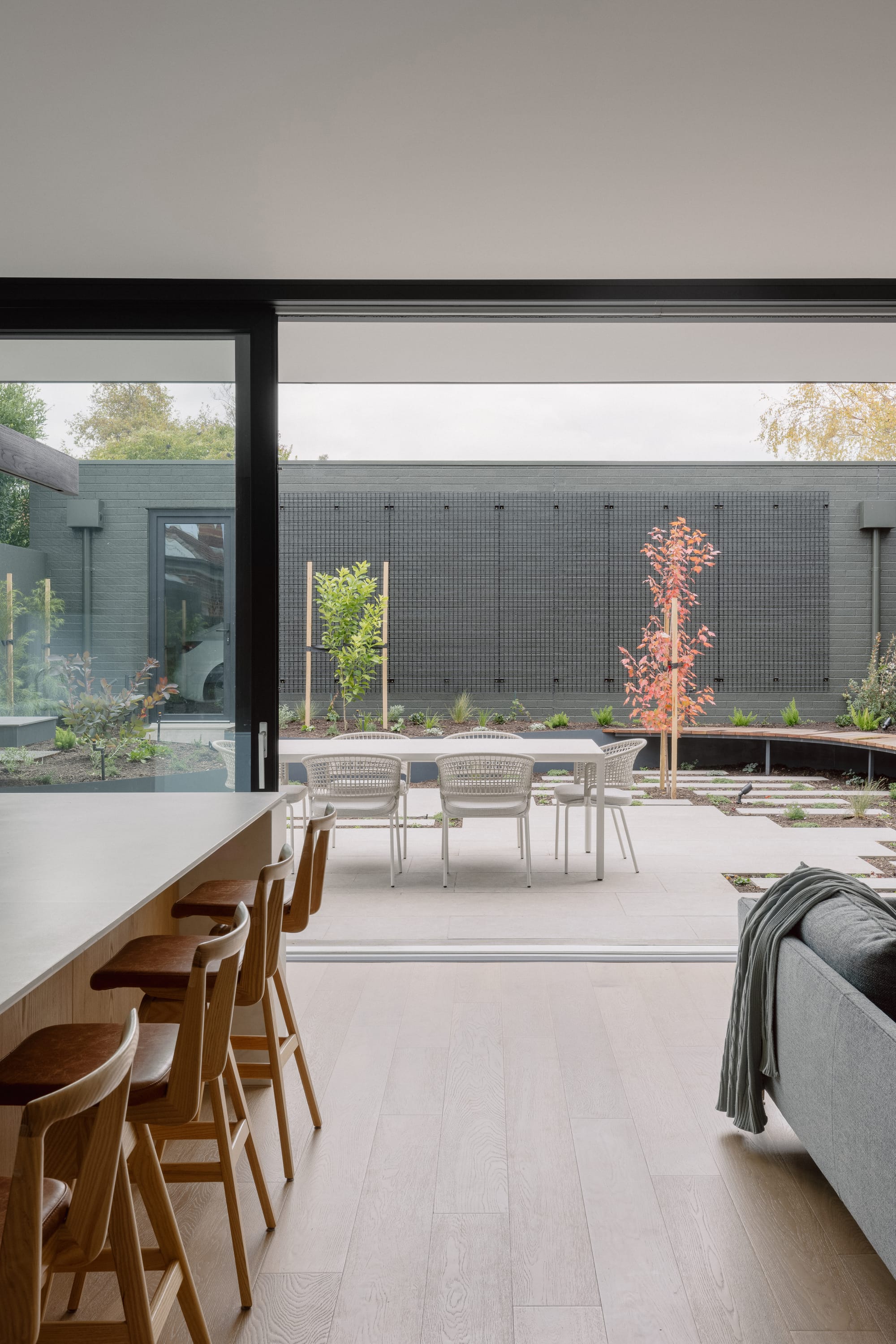 Auburn Residence by Chan Architecture. Photography by Elise Scott. Large sliding glass doors in kitchen and living room opening onto paved outdoor area with white table, black brick walls and plants. 