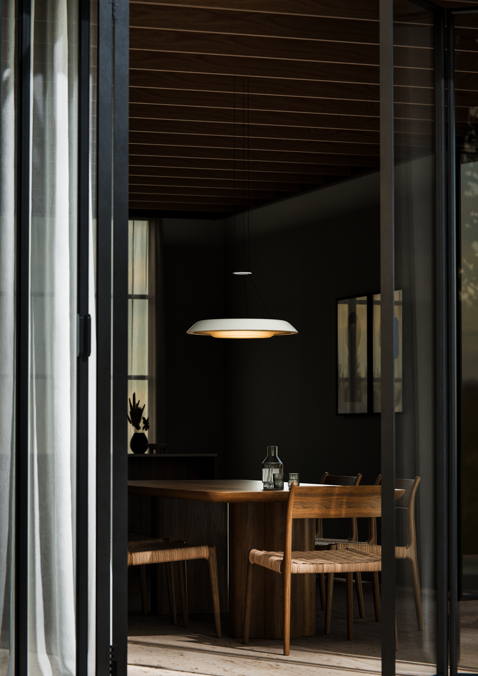Husk Collection By South Drawn. Photography by Reannon Smith. A warm pendant light hovers over a timber dining setting, framed by soft curtains and sliding glass doors.