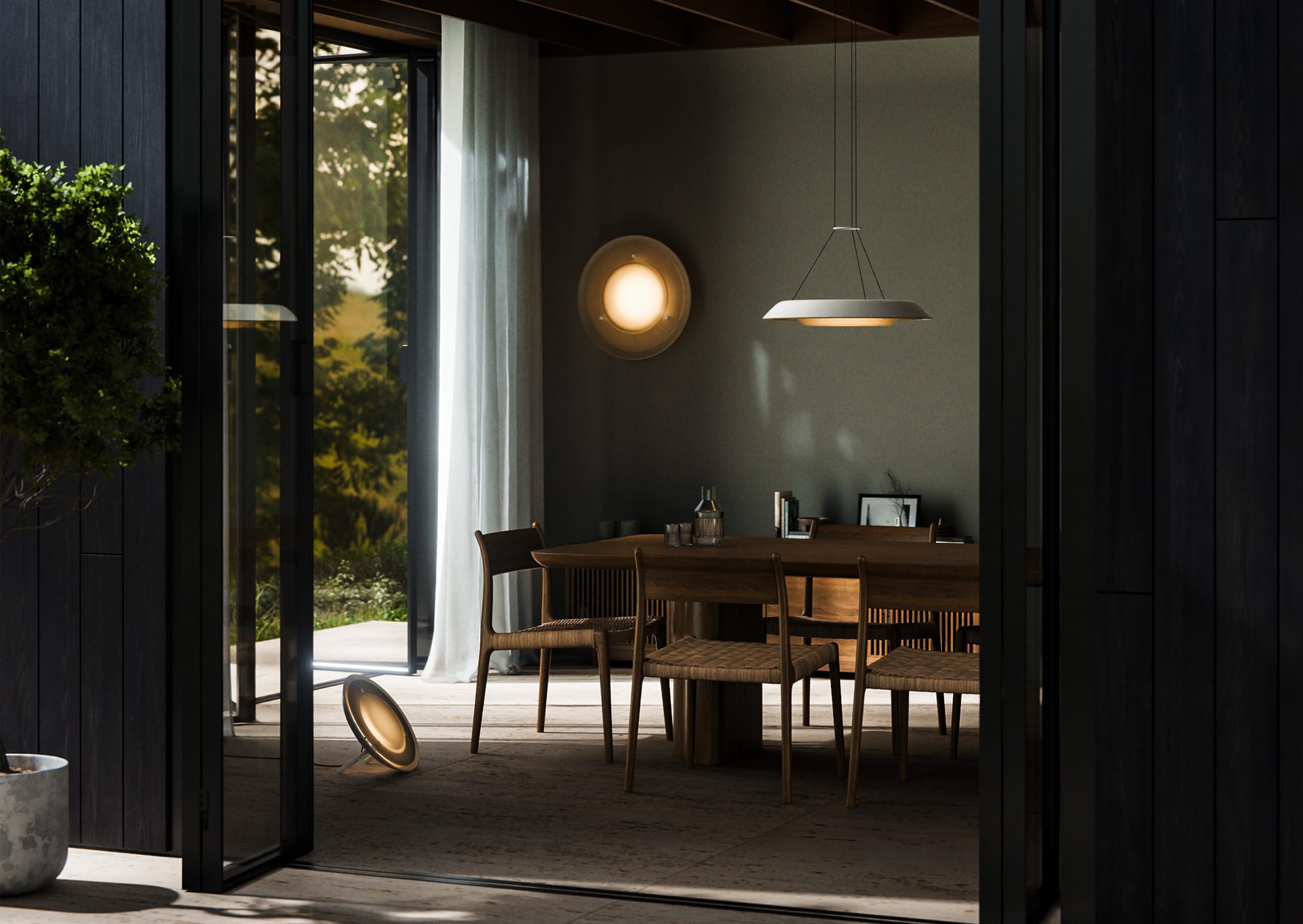 Husk Collection By South Drawn. Photography by Reannon Smith. Framed by open doors, the warm glow of the Husk Collection softly illuminates a timber dining setting, blurring the line between indoors and out.