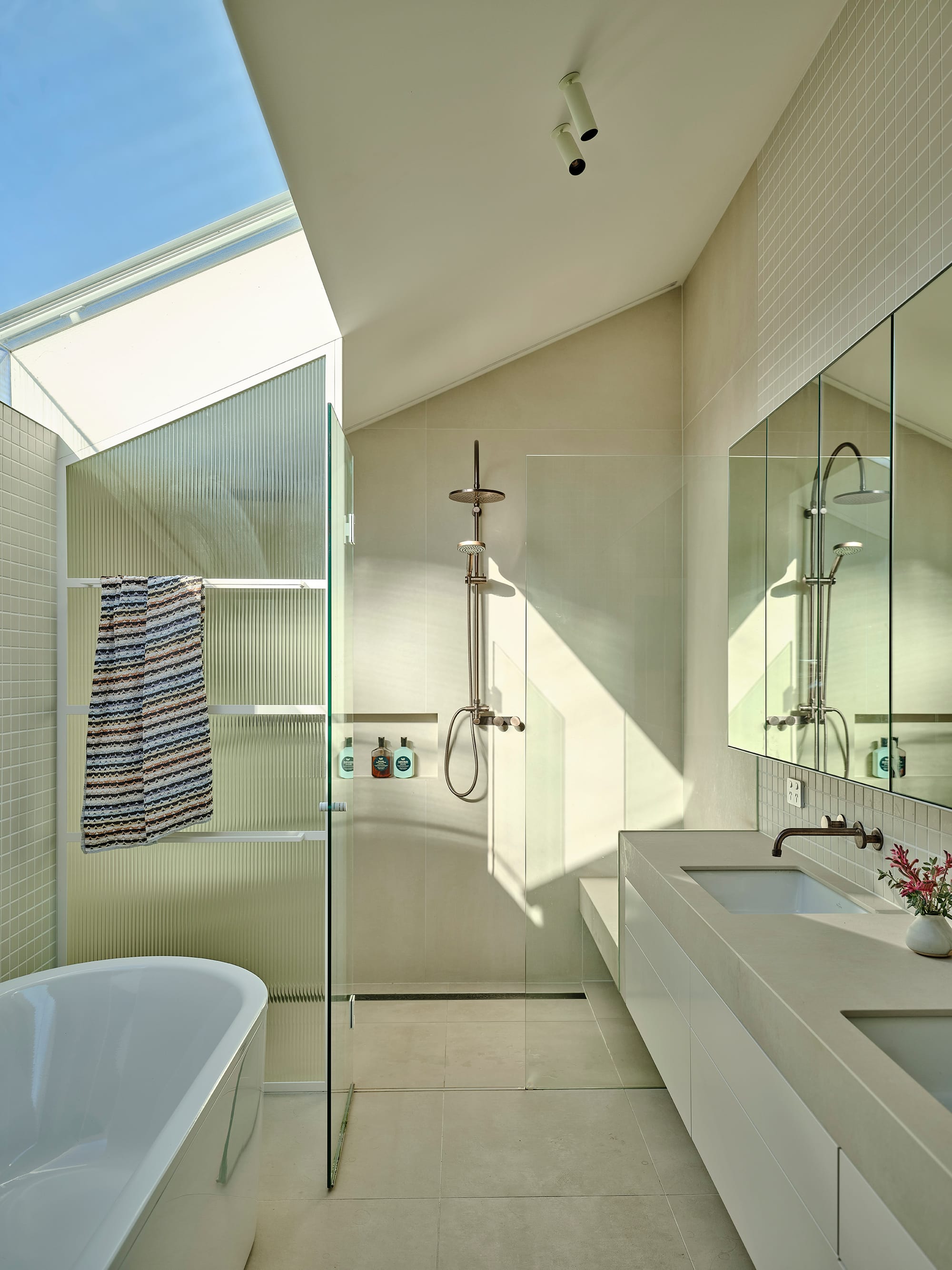 Salmon House by True Story. Photography by Dean Bradley. Light-filled bathroom with freestanding tub, dual sinks, and skylit shower framed by fluted glass.