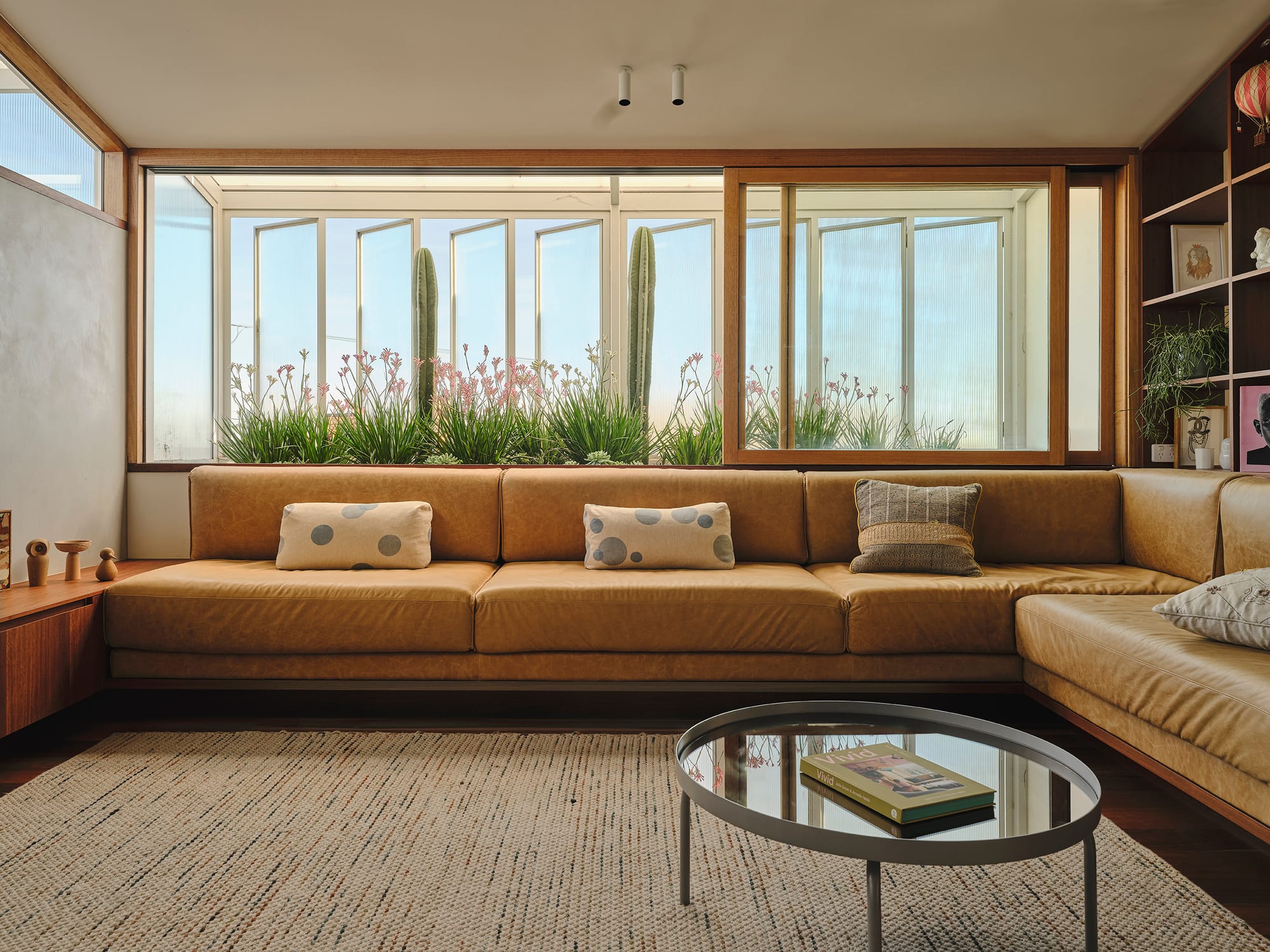 Salmon House by True Story. Photography by Dean Bradley. Sunken lounge with tan leather seating, cactus-framed windows, and warm timber shelving for a desert-inspired retreat.