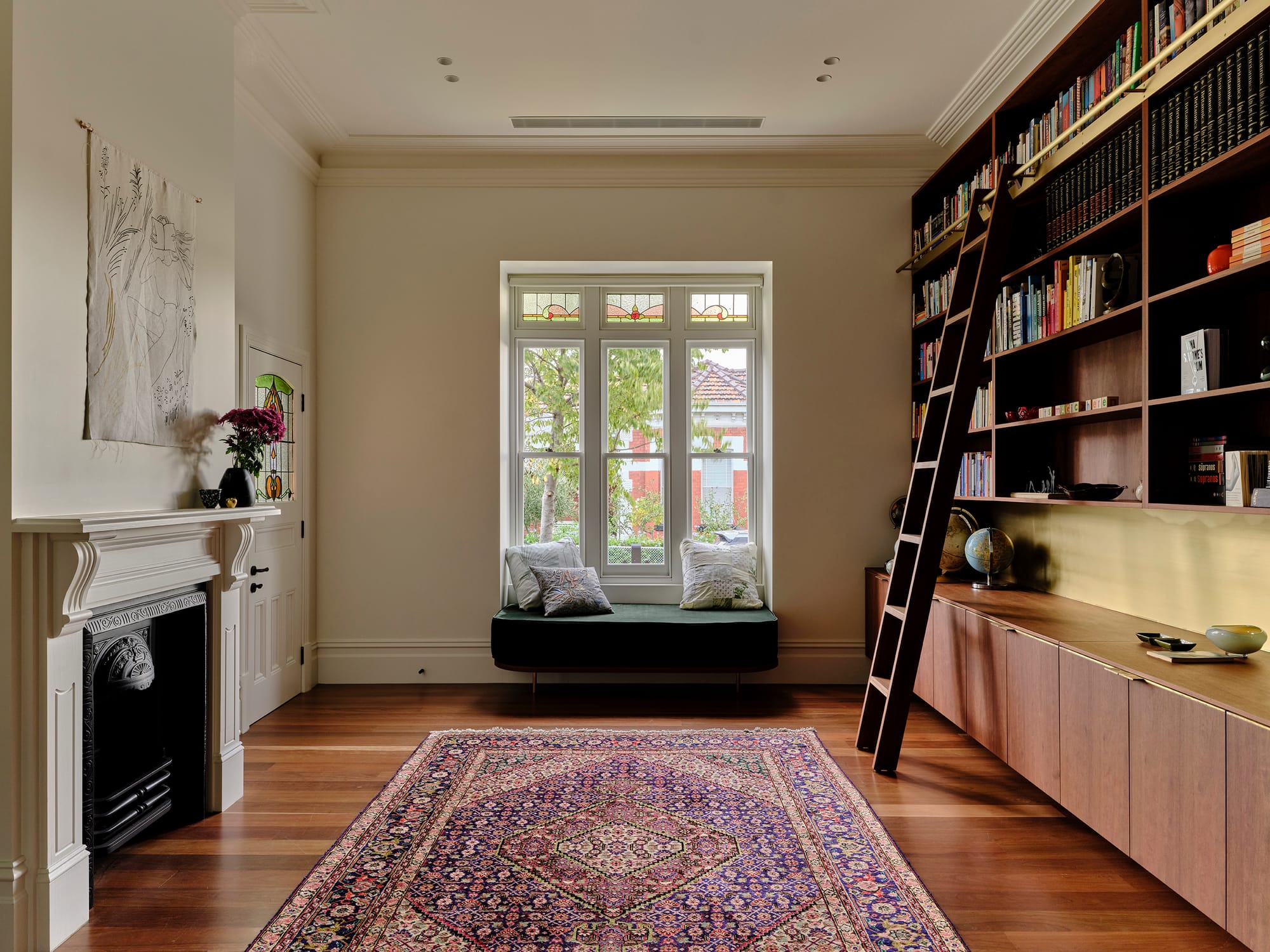 Salmon House by True Story. Photography by Dean Bradley.Elegant home library with built-in shelving, rolling ladder, and a deep window seat, layered with classic detailing and a Persian rug.