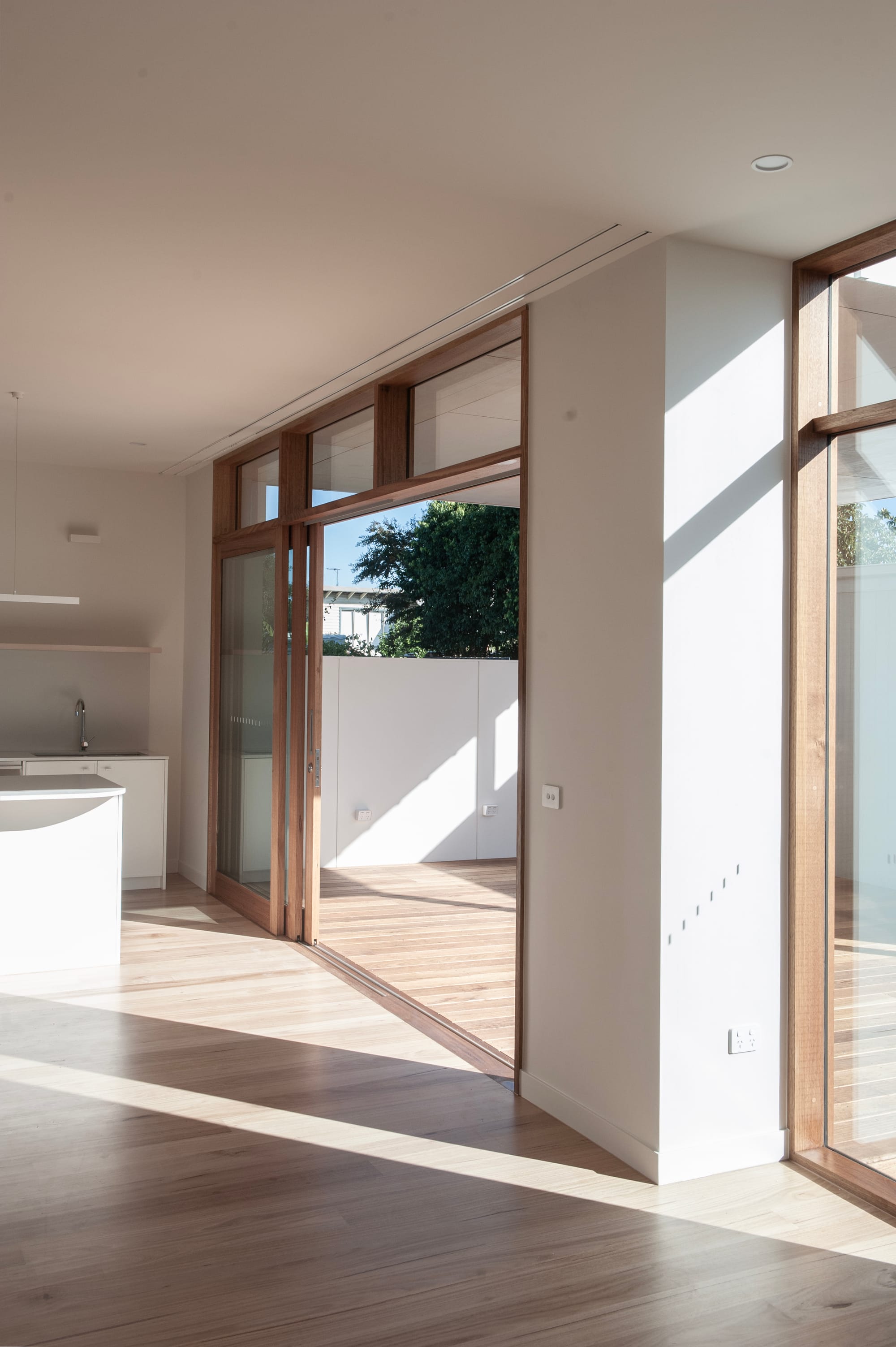 Sunset Joinery. Photography by Sunset Joinery.Bright interior with light timber flooring, full-height glass doors framed in timber, and seamless flow from kitchen to outdoor decking under clear daylight.