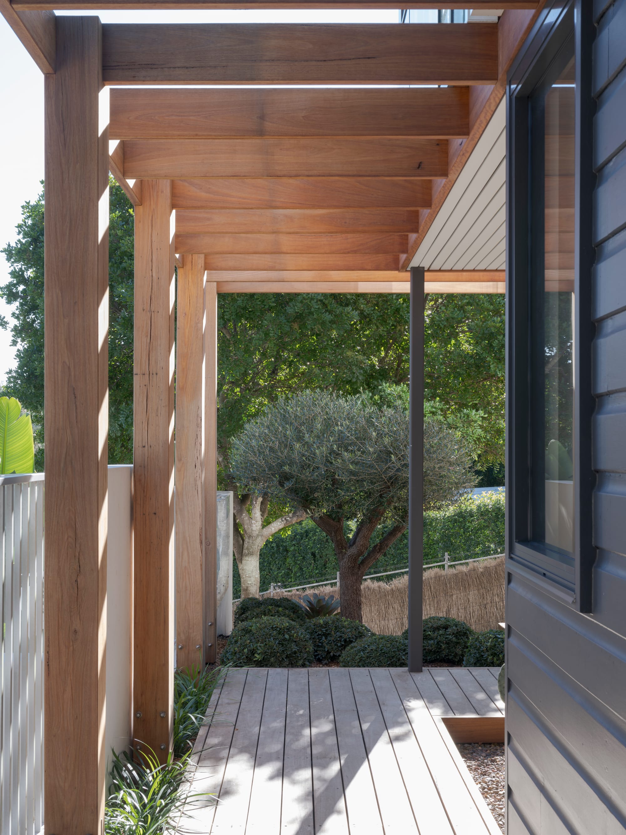 Three Points House by BIJL Architecture. Photography by Tom Ferguson.Timber pergola over a decked walkway beside a house, with landscaped garden and mature trees in the background.