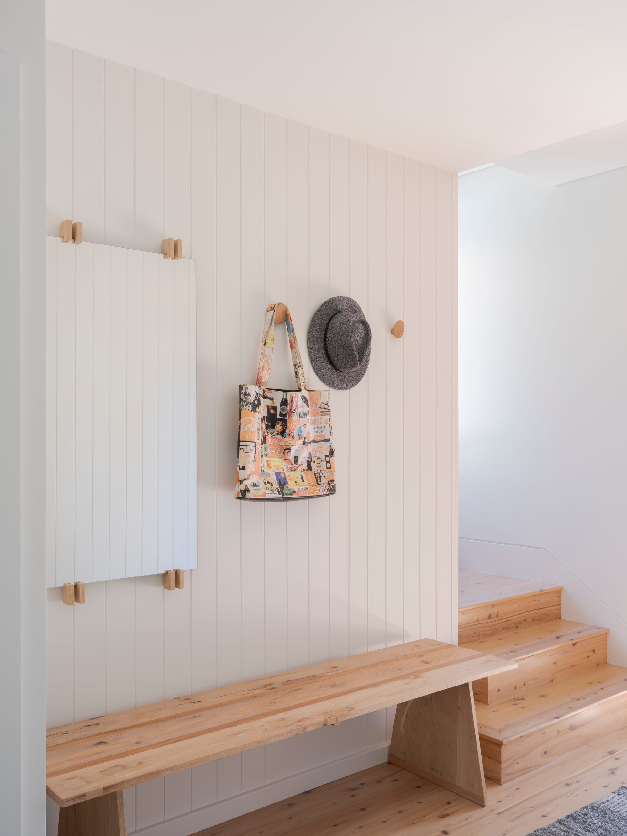 Three Points House by BIJL Architecture. Photography by Tom Ferguson.Entry nook with timber bench, vertical wall panelling, mirror, and pegs holding a hat and patterned tote bag.