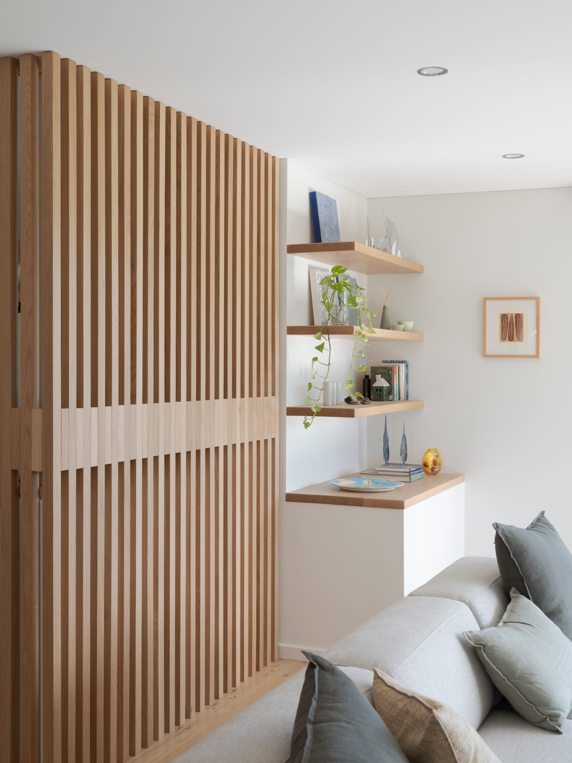Three Points House by BIJL Architecture. Photography by Tom Ferguson. Timber batten screen beside floating shelves styled with books, ceramics, and a trailing plant in a soft-toned living room.