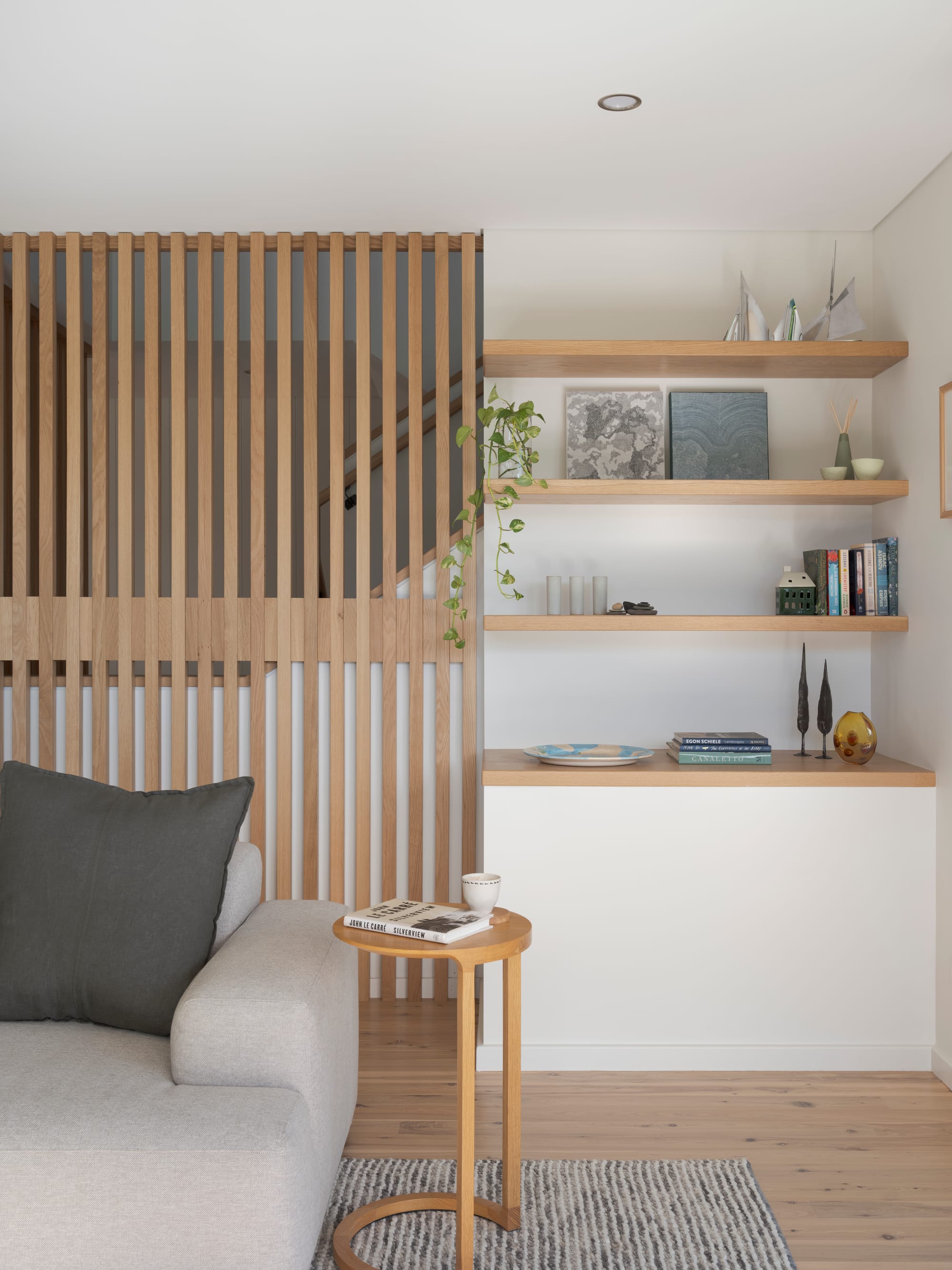 Three Points House by BIJL Architecture. Photography by Tom Ferguson.Timber batten screen beside floating shelves styled with books, ceramics, and plants above a light-toned bench and soft grey sofa.