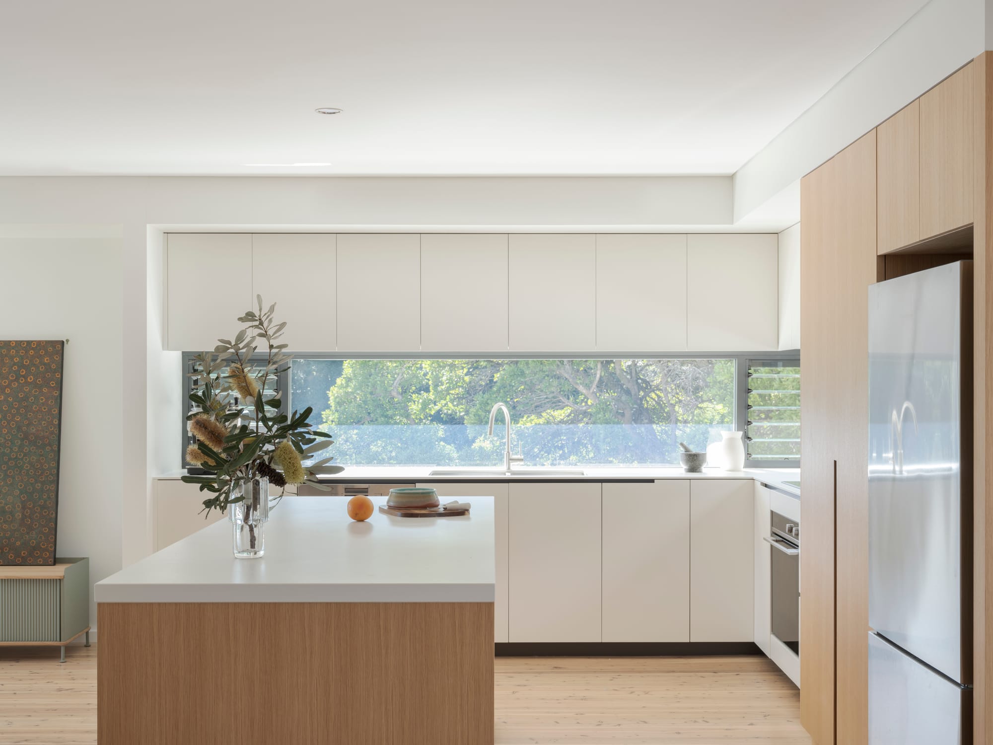 Three Points House by BIJL Architecture. Photography by Tom Ferguson.Minimal kitchen with white cabinetry, timber accents, island bench and horizontal window bringing in garden views.