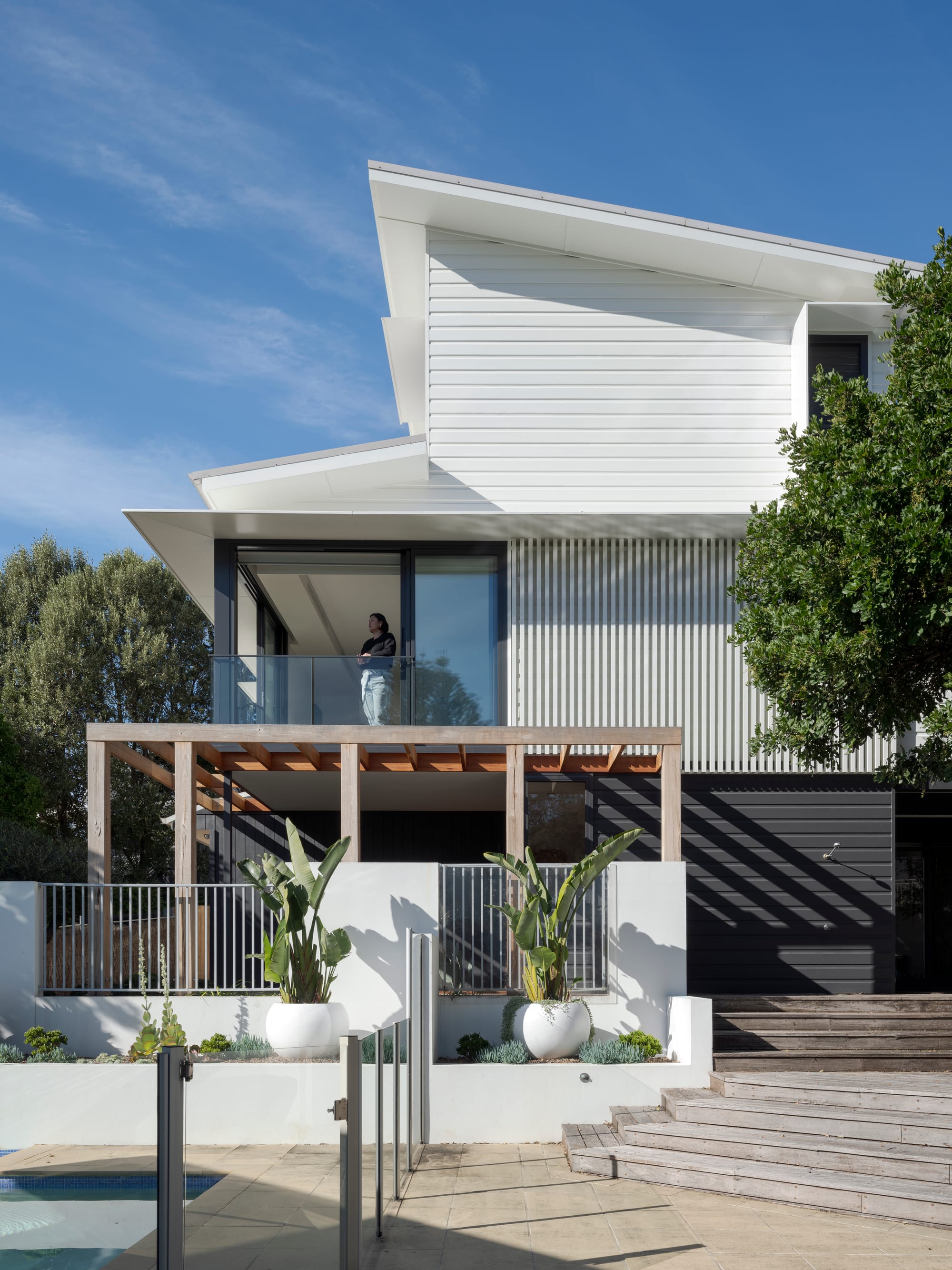 Three Points House by BIJL Architecture. Photography by Tom Ferguson.Modern white house with timber pergola, balcony, and landscaped poolside area featuring large potted plants and tiered timber steps.