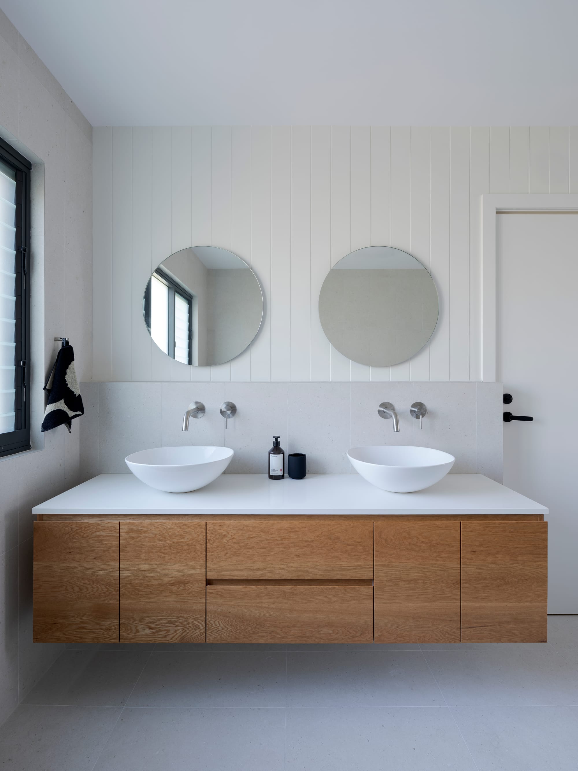 Three Points House by BIJL Architecture. Photography by Tom Ferguson.Minimalist bathroom with timber vanity, twin vessel sinks, round mirrors, and soft natural light.