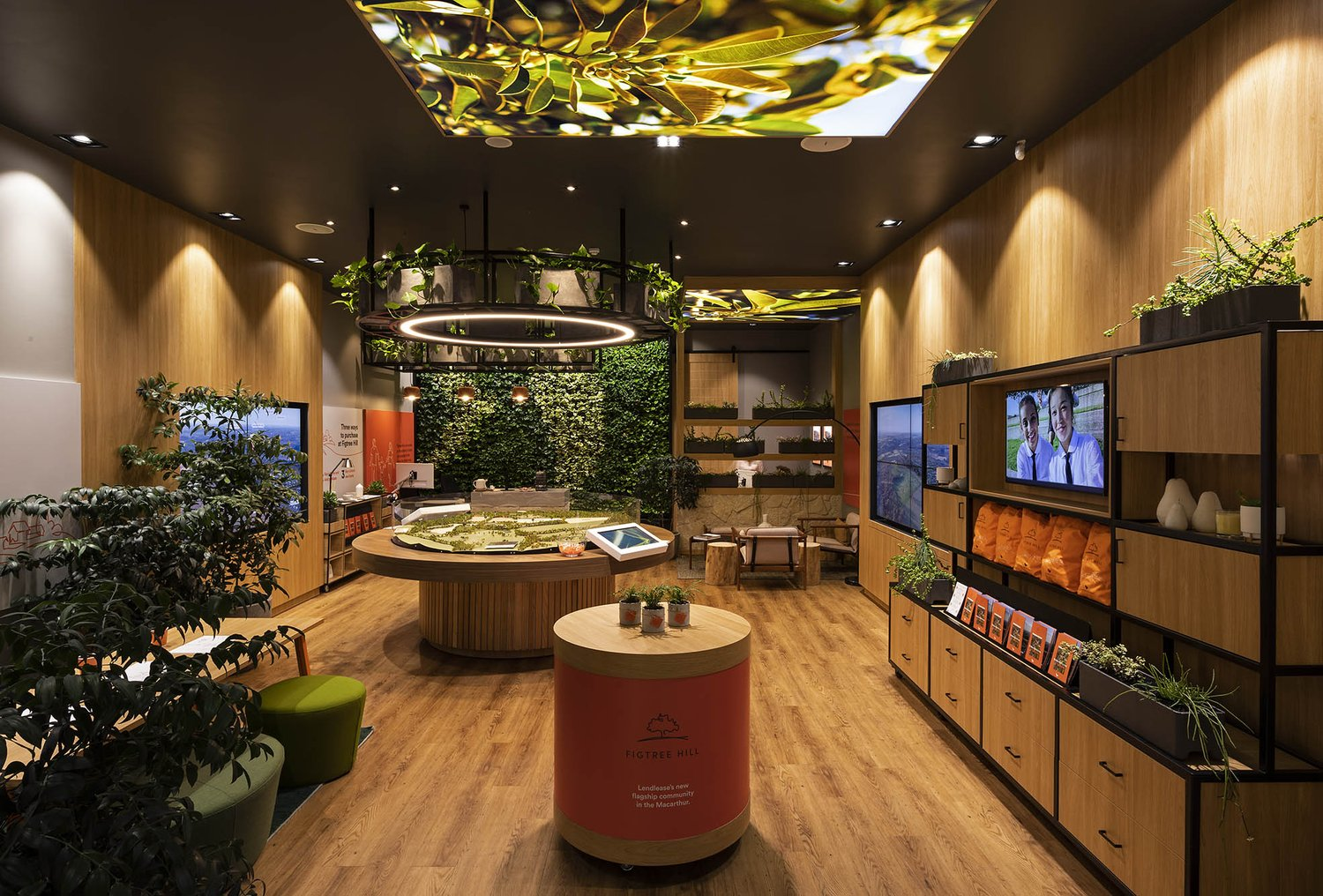 Figtree Hill Sales Suite by The Great Indoors. Photography by Andrew Worssom. Modern sales or display suite with a central architectural model, vertical garden wall, timber finishes, integrated screens, and lush greenery enhancing the interior atmosphere.