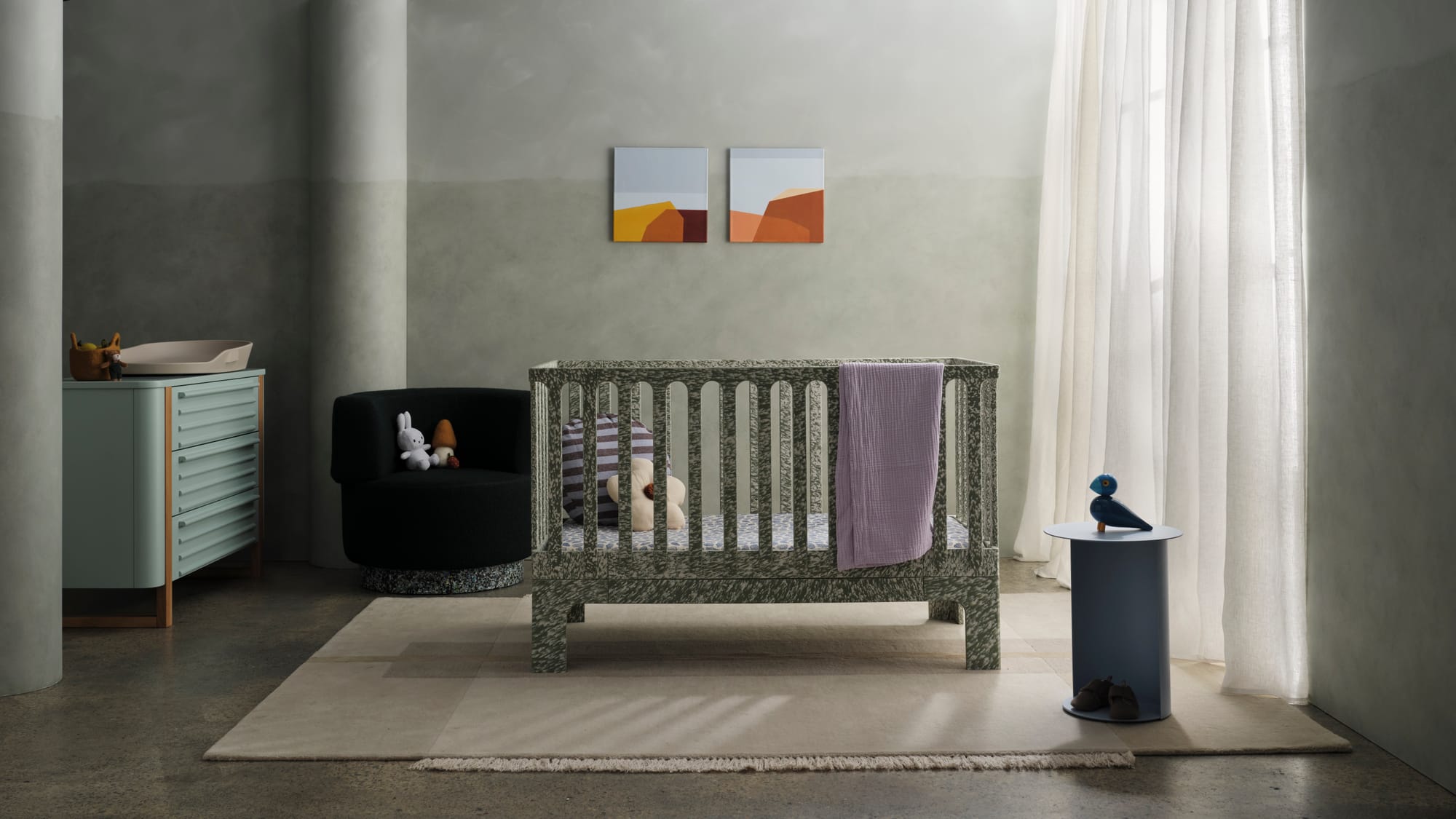 Archie Cot by Seena x Defy in Sage Spray. Green and white speckled cot in room with grey marbled walls and concrete floors. 