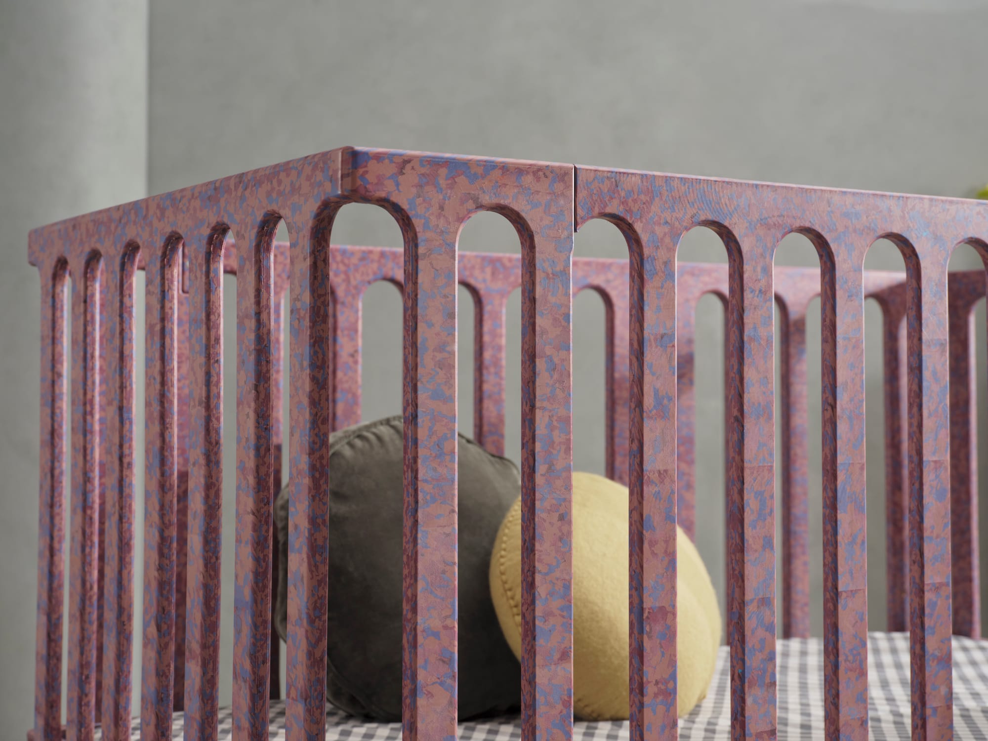 Archie Cot by Seena x Defy in Plum. Cot with pink and purple speckles with gingham mattress cover and green and olive round cushions. 