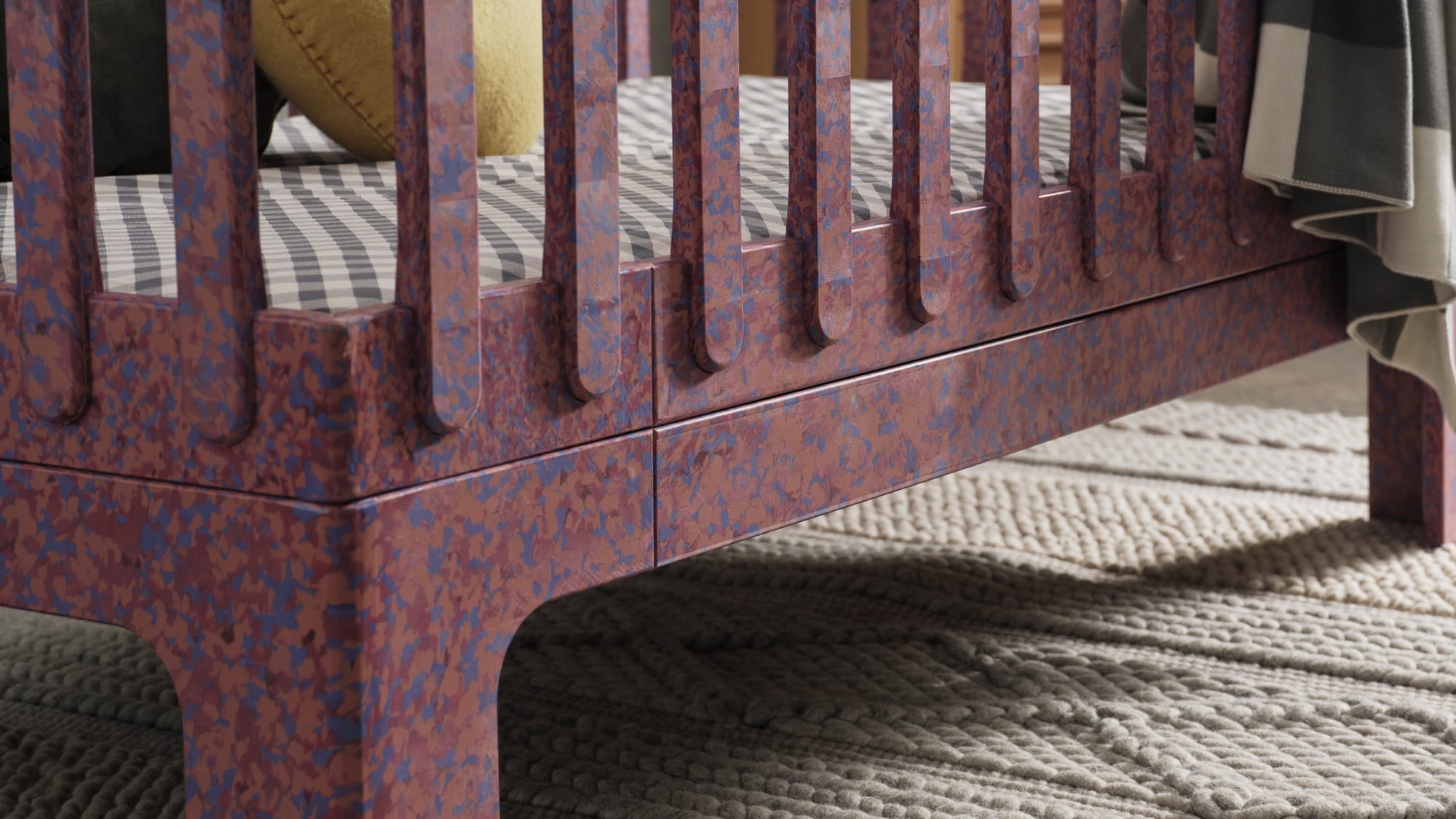 Archie Cot by Seena x Defy in Plum. Purple cot with pink and purple speckles, white knit rug and black and white plaid mattress cover. 