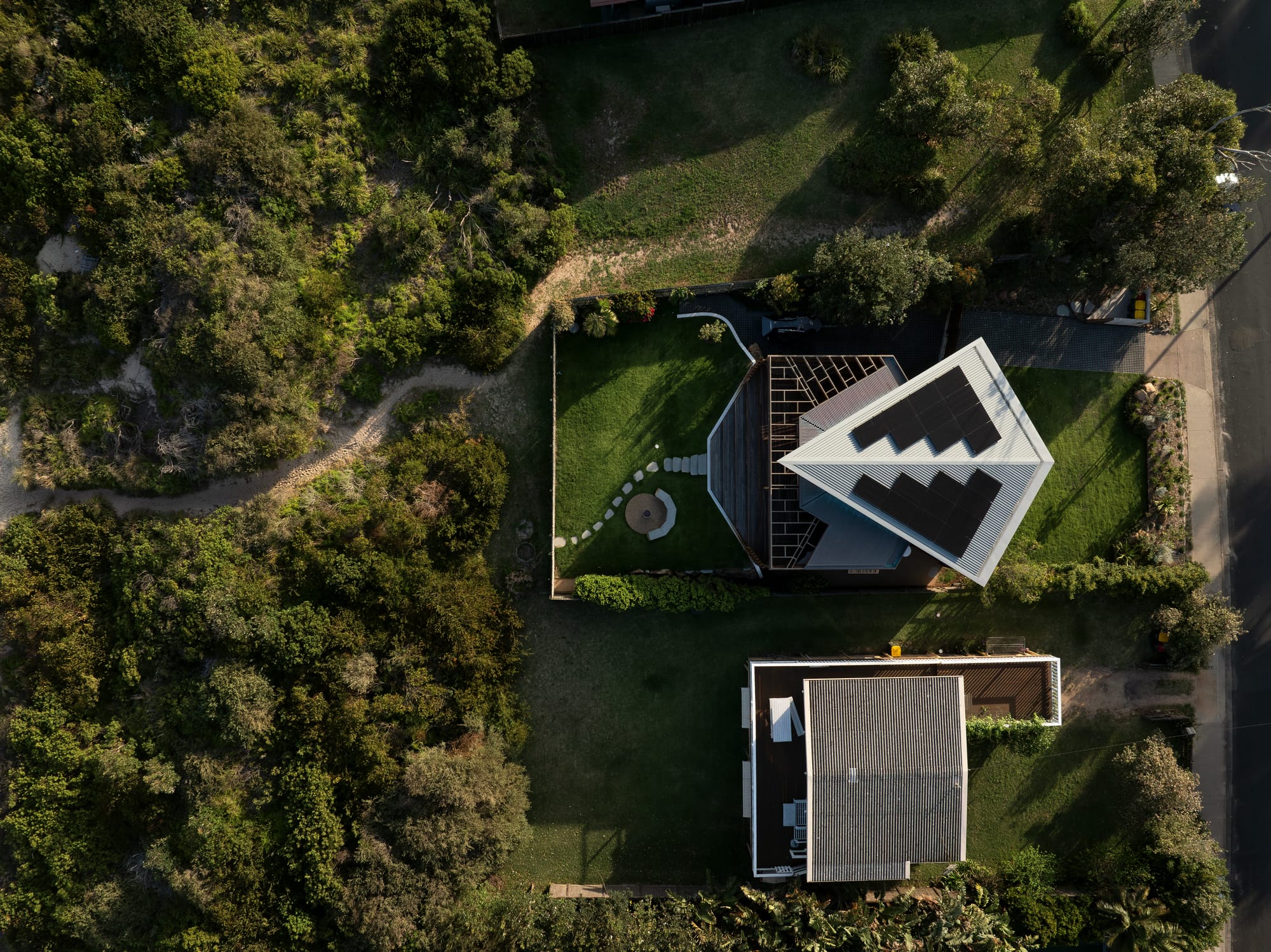 Cake House by Alexander Symes Architect. Photography by Barton Taylor.  Aerial view of residential home with kite-shaped roof, grassy backyard and front yard and sand path leading through the scrub to the beach. 