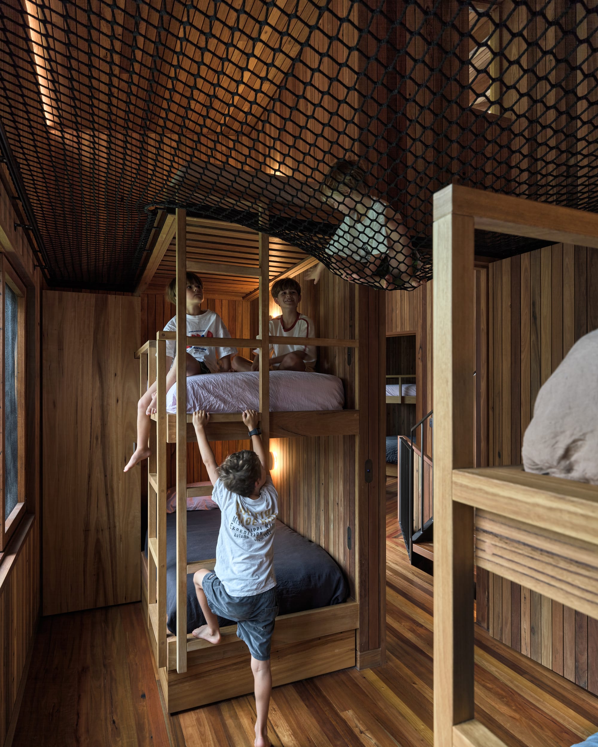 Cake House by Alexander Symes Architect. Photography by Barton Taylor.  Childrens bedroom with timber floors, walls and bunk beds, and a netted ceiling, with multiple children playing. 