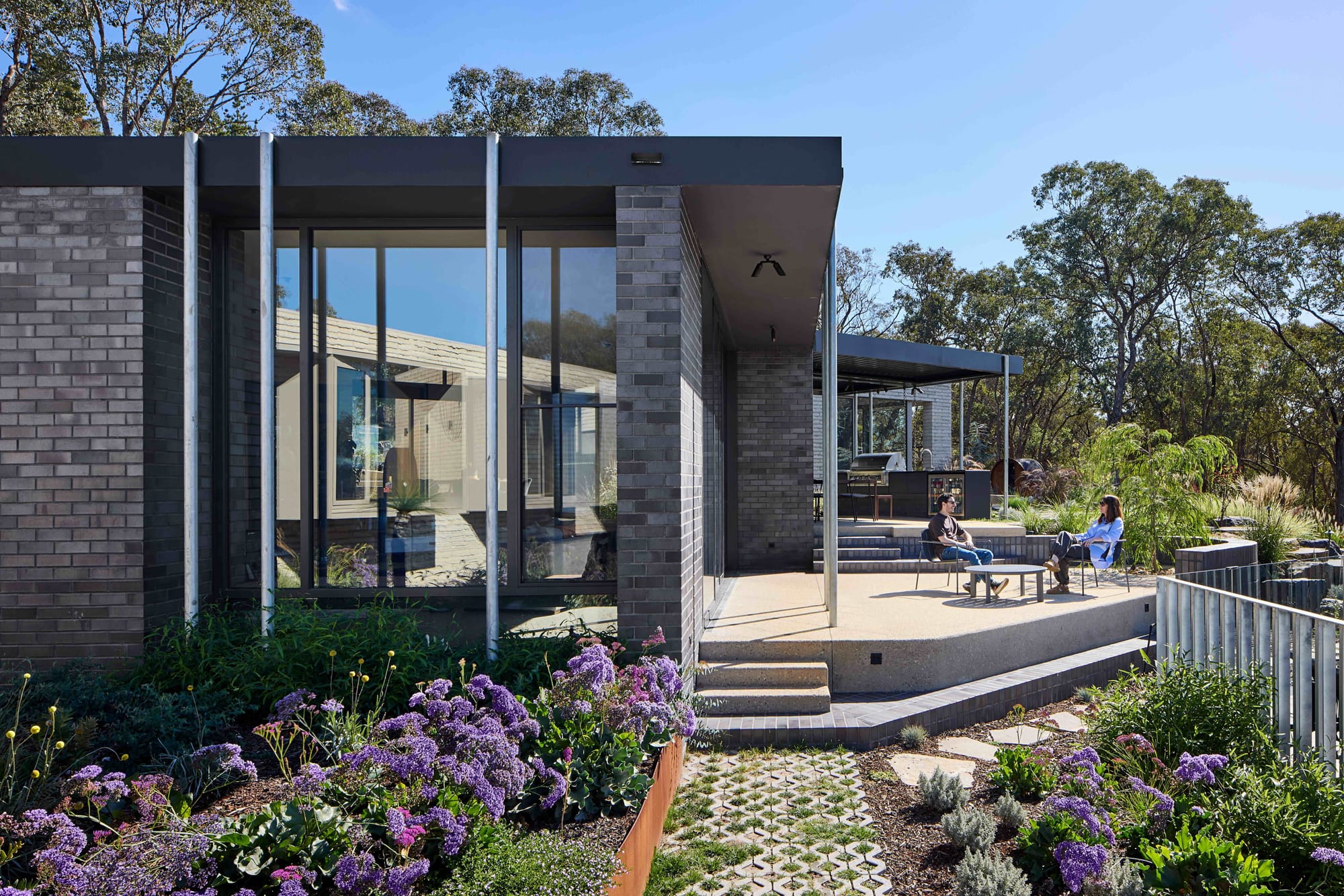 Korinda House by BENT Architecture. Photography by Tatjana Plitt. Exterior of dark brick home with elevated patio, surrounded by native plant gardens. 