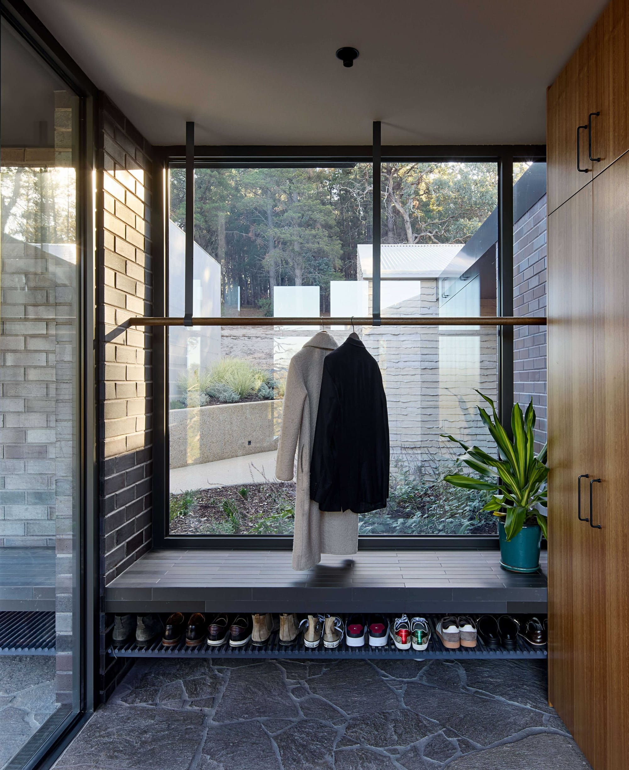 Korinda House by BENT Architecture. Photography by Tatjana Plitt. Entry to home with timber cabinetry, granite paver floors and hanging rail and shoe rack. 