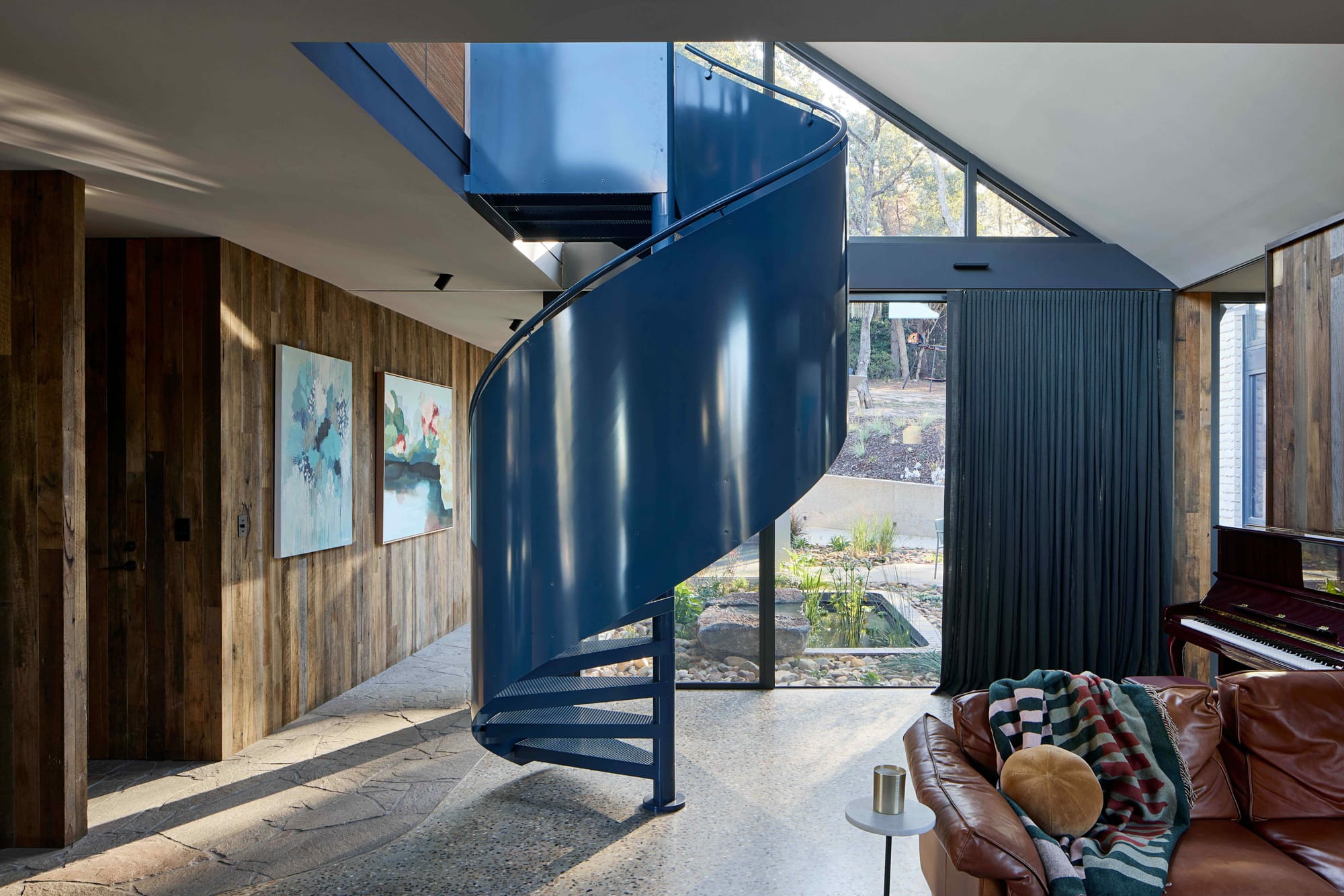 Korinda House by BENT Architecture. Photography by Tatjana Plitt. Navy spiral staircase in living room, alongside timber clad gallery wall to the left. 