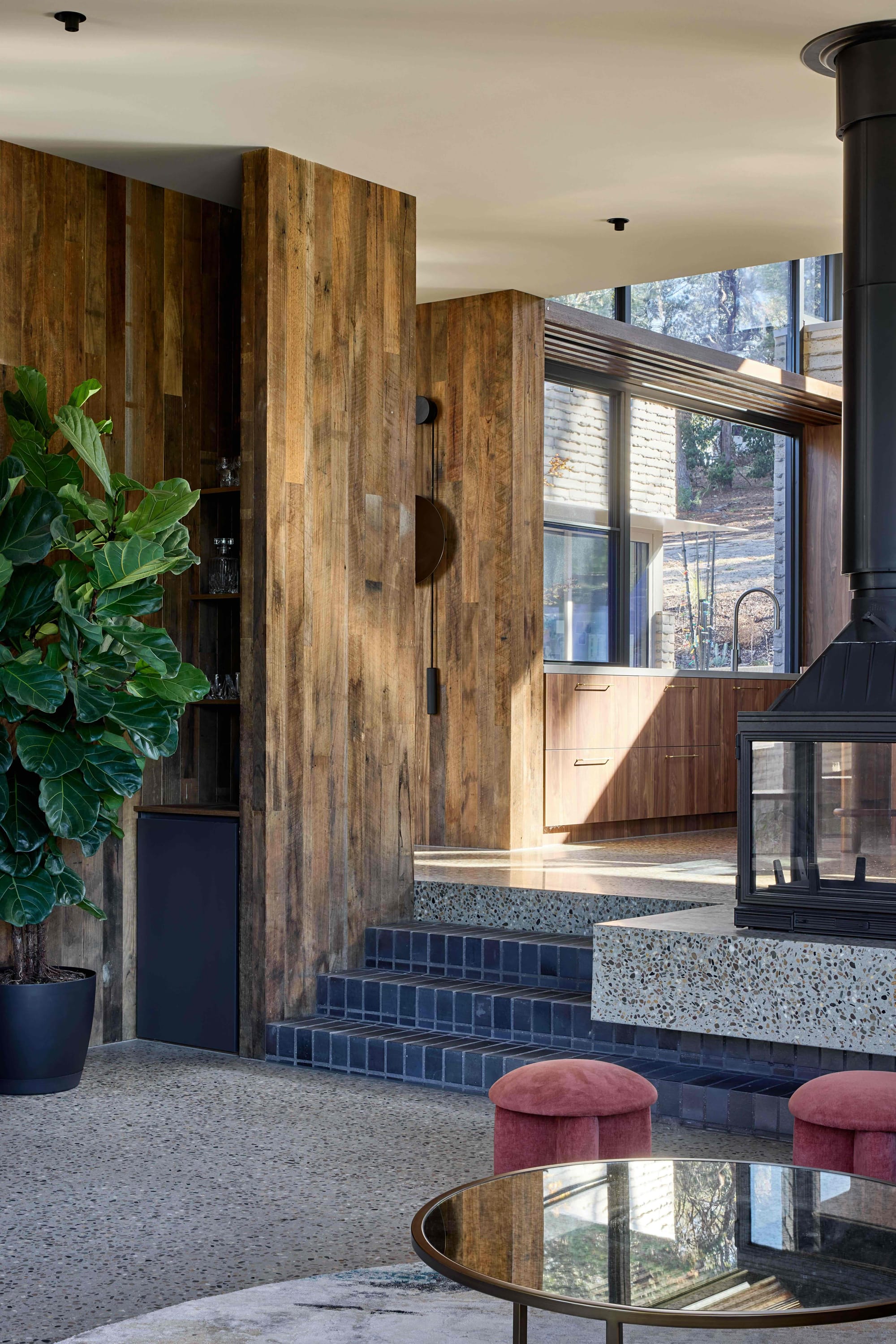 Korinda House by BENT Architecture. Photography by Tatjana Plitt. Sunken living space with dark brick stairs, polished concrete stairs, marble fireplace plinth and pink velvet stools. 