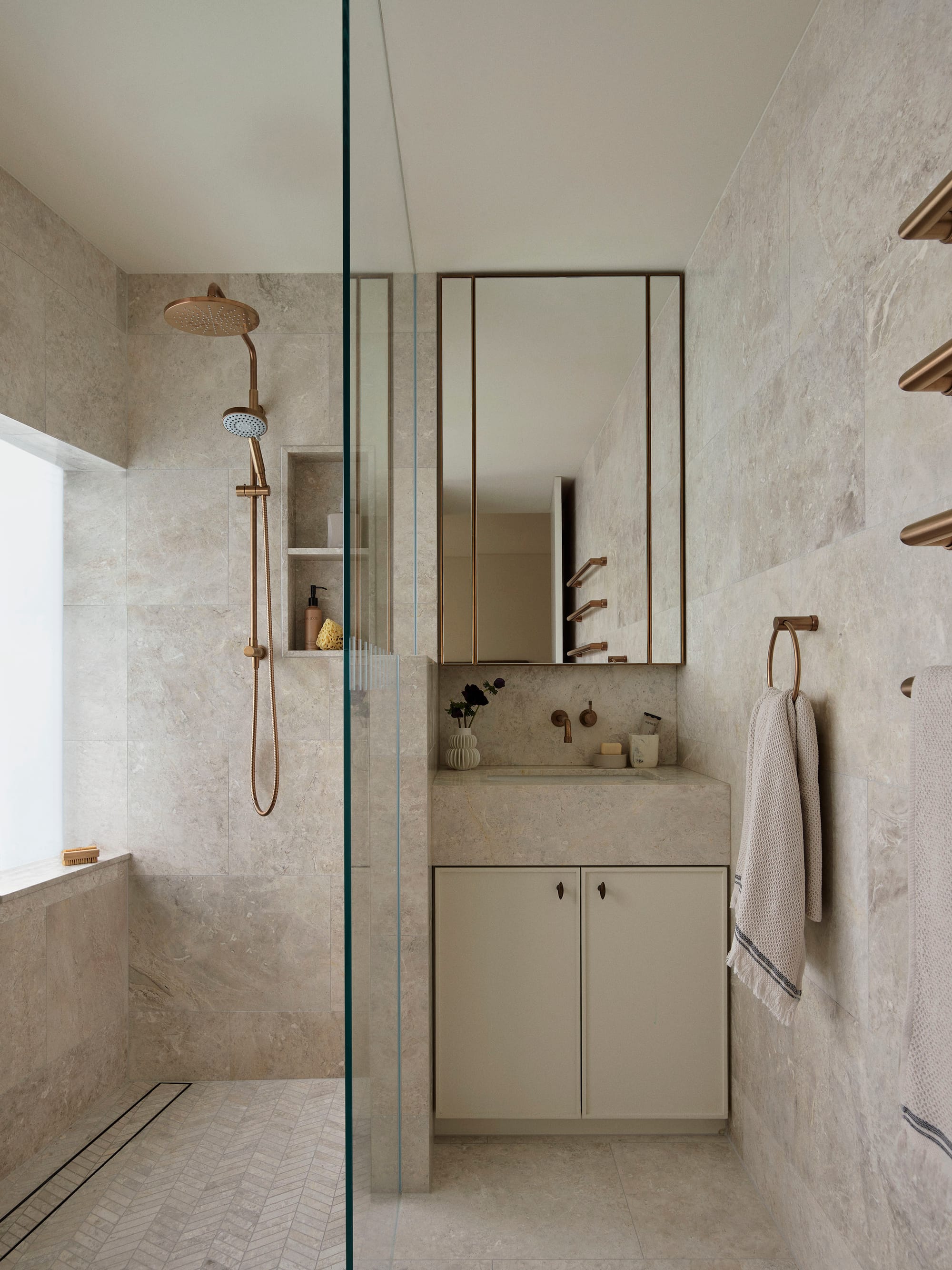 Bundarra Penthouse by Marylou Sobel Interior Design. Photography by Anson Smart. Beige marbled bathroom with glass shower screen and copper details. 