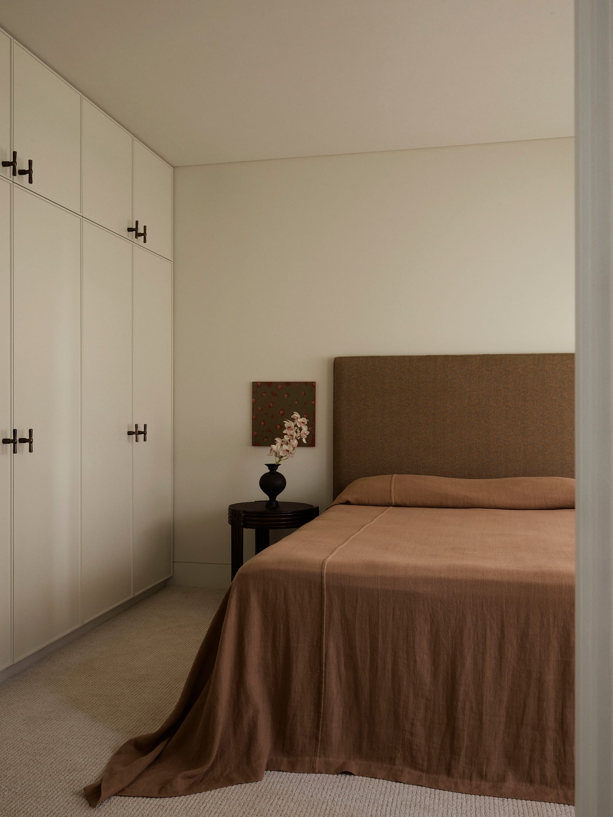 Bundarra Penthouse by Marylou Sobel Interior Design. Photography by Anson Smart. Bedroom with terracotta bed linen, full height white wardrobes and beige carpet. 