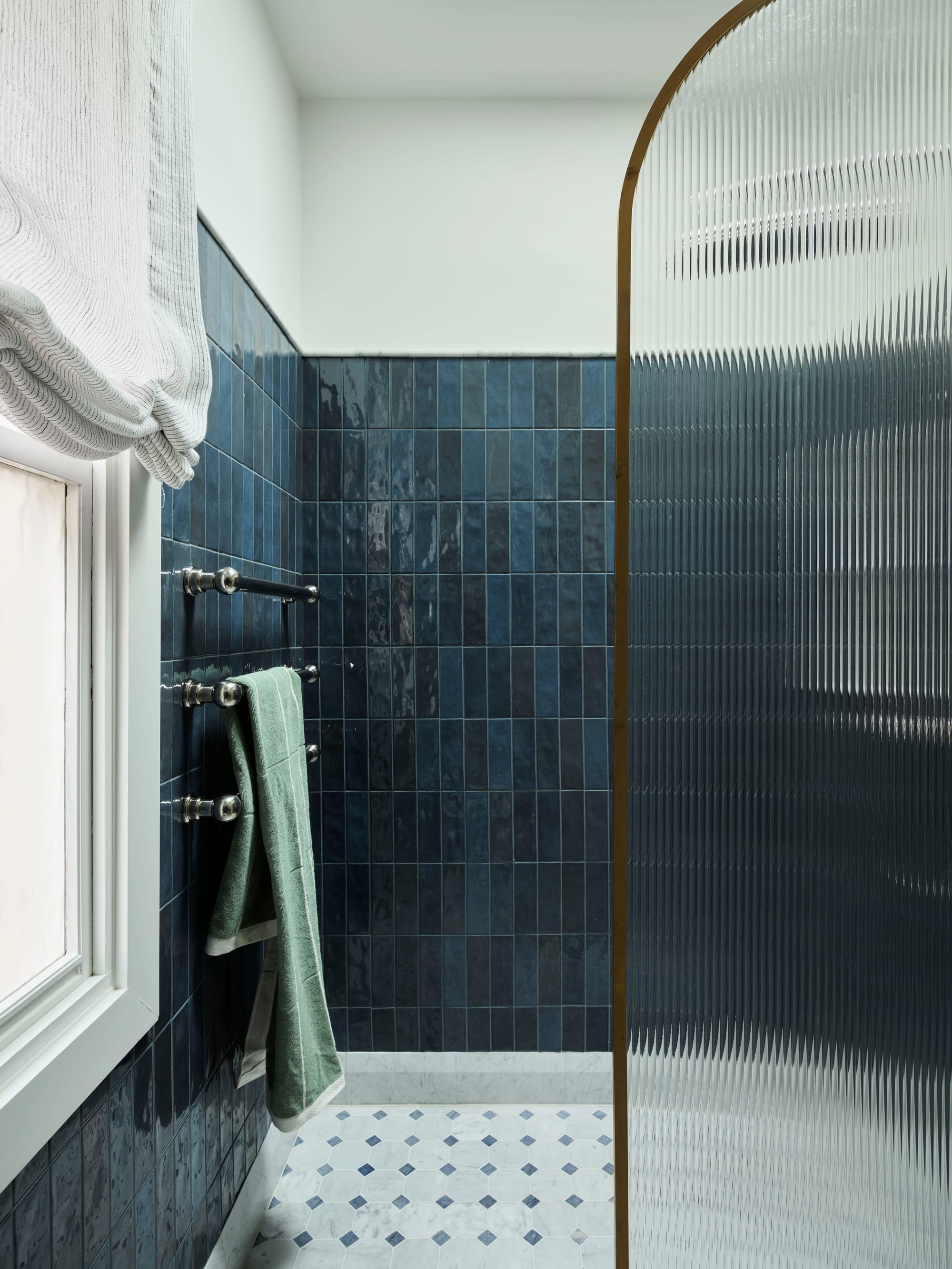 Ferris Street by Marylou Sobel Interior Design. Photography by Anson Smart. Bathroom with dark blue subway tiles, fluted glass shower screen, silver towel rails and white and blue mosaic floor tiles. 