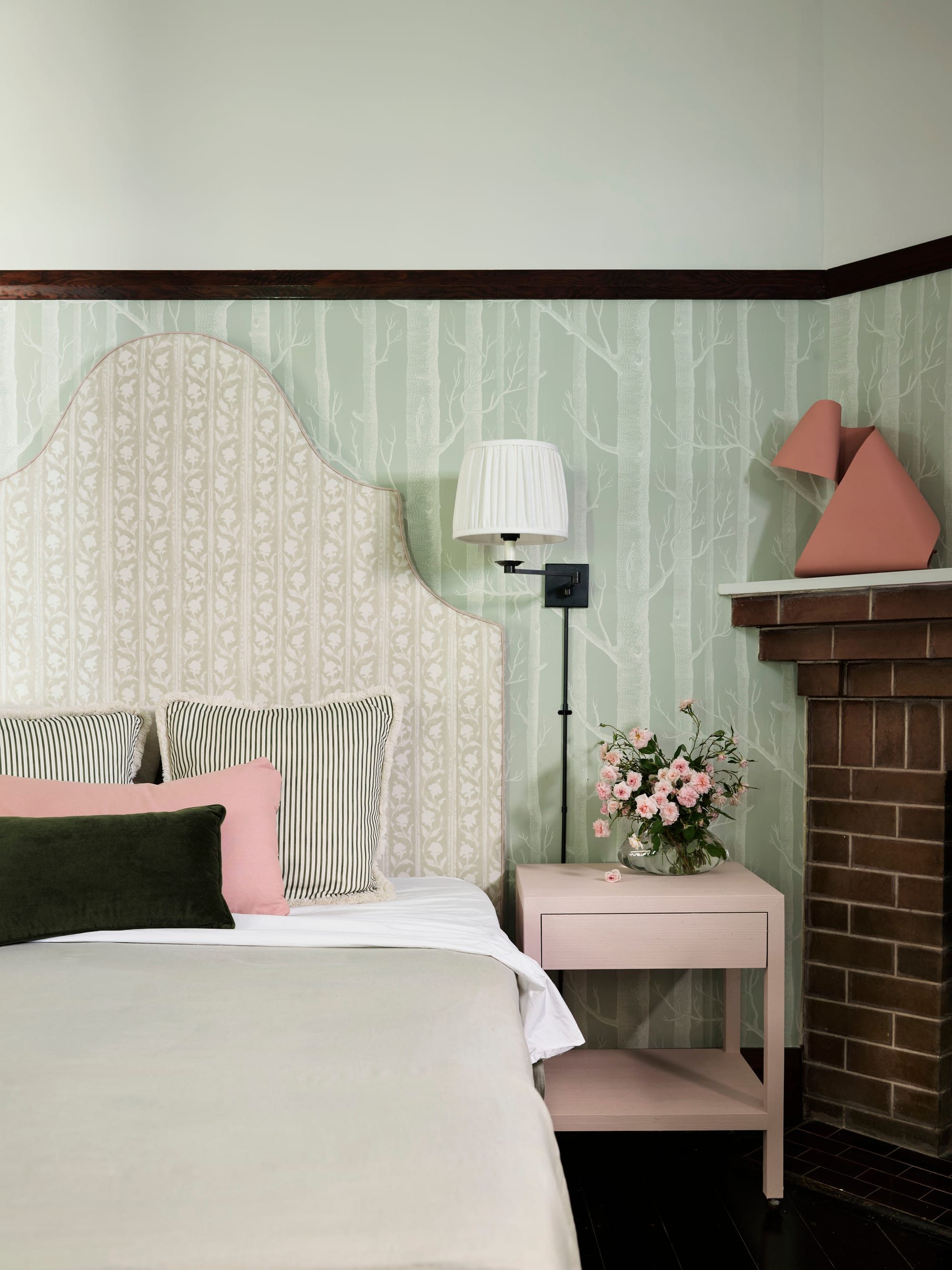 Ferris Street by Marylou Sobel Interior Design. Photography by Anson Smart. Bedroom with light green wallpaper, fabric headboard, light green and pale pink soft furnishings and brick fireplace. 